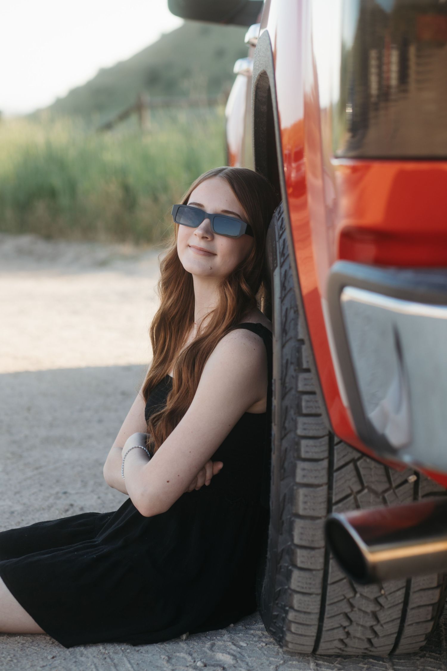 Boise senior photos of high school girl wearing sunglasses sitting by red truck tire in golden hour outdoor session