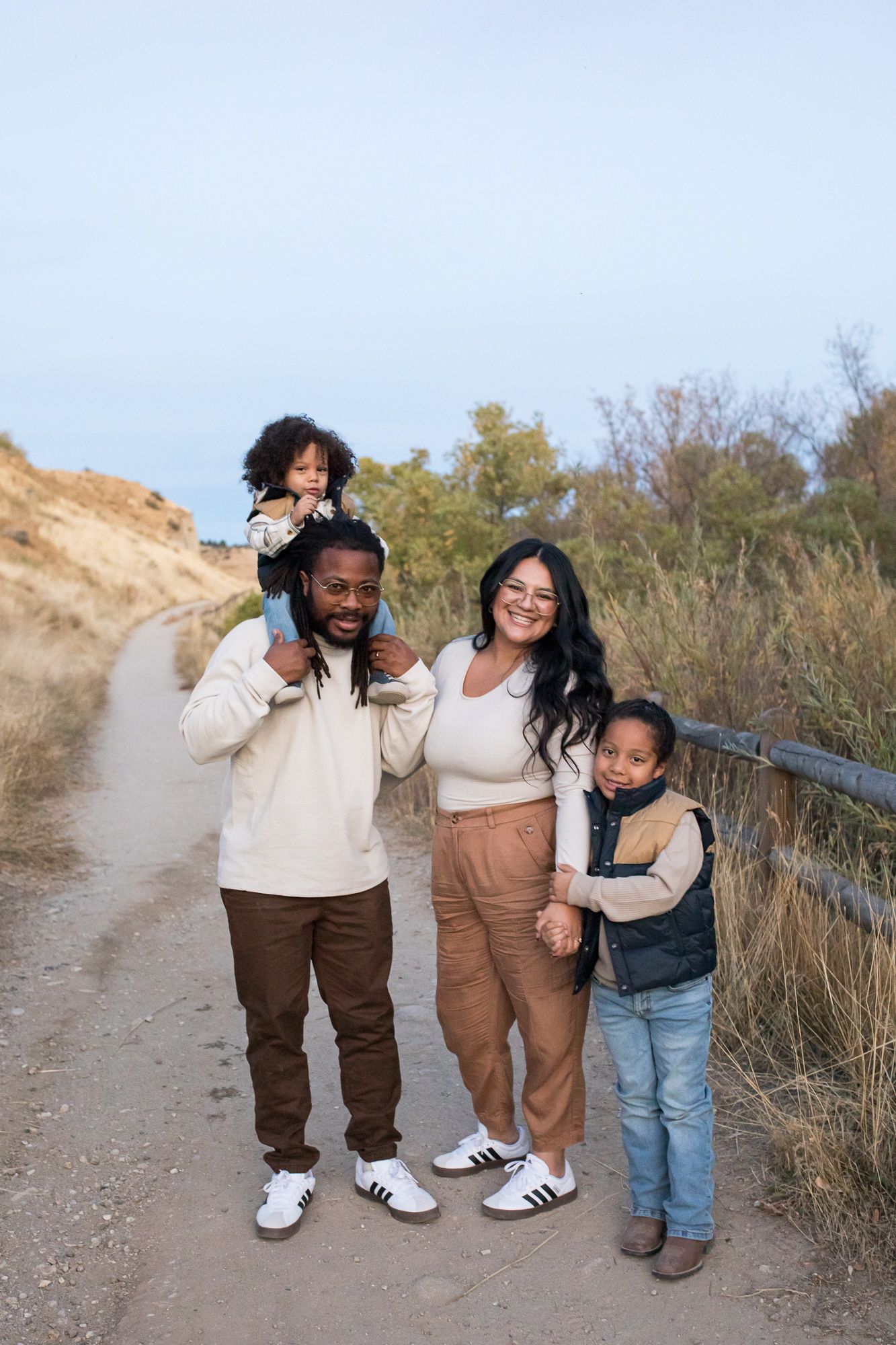 A family enjoys a hike together on a dirt trail surrounded by nature on a sunny day - lifestyle family photos in Boise