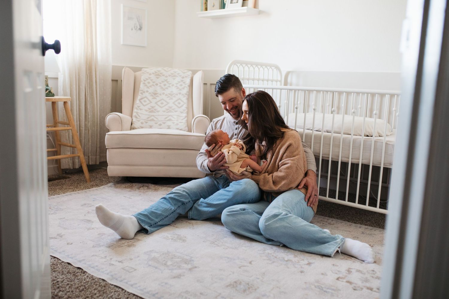 Parent and baby play together on a cozy gray carpet in a bright nursery with white furniture- lifestyle in-home newborn photos Boise