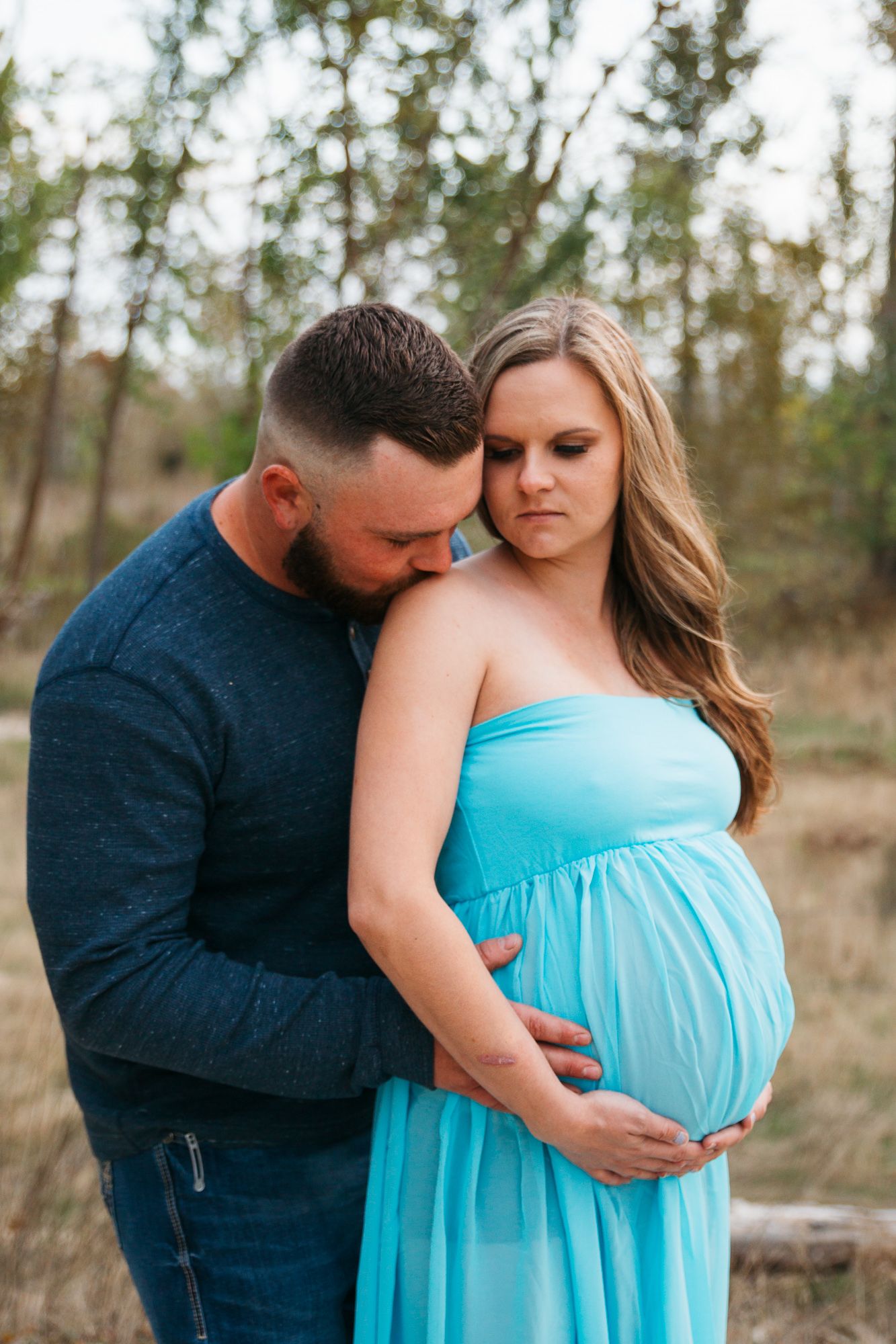 A couple in a natural outdoor setting share an intimate moment, with the person wearing a flowing turquoise maternity dress. - Eagle Idaho