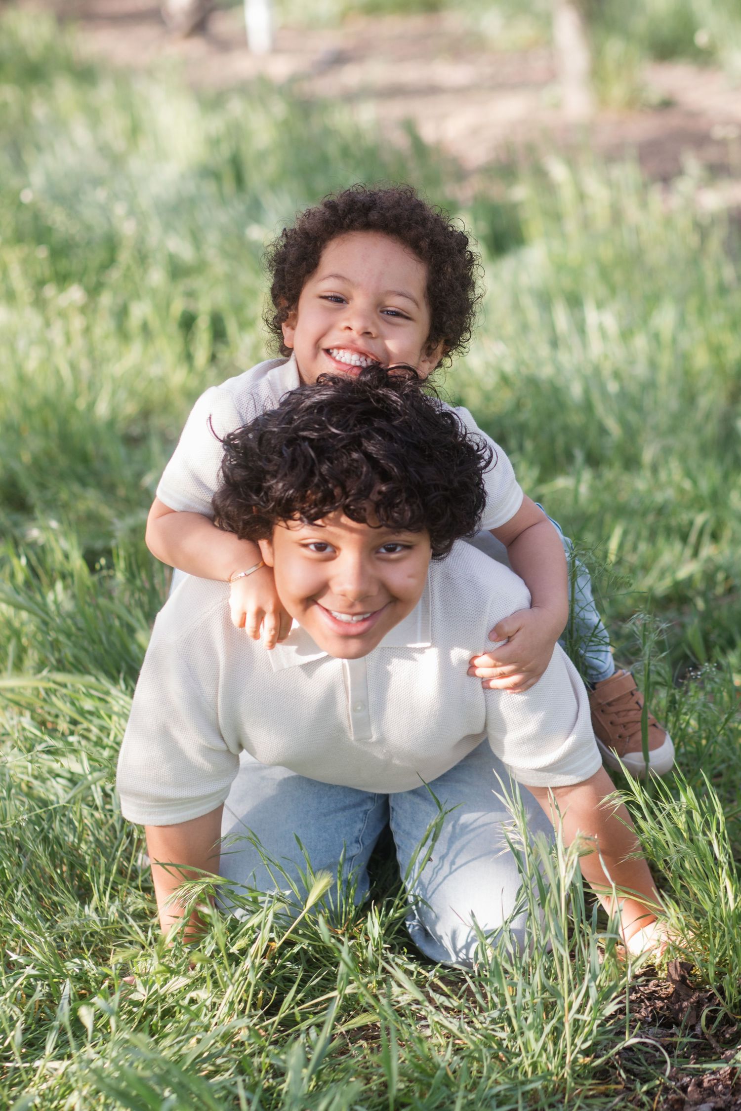 Two brothers laughing and playing piggyback under spring blossoms during family session in Caldwell Idaho