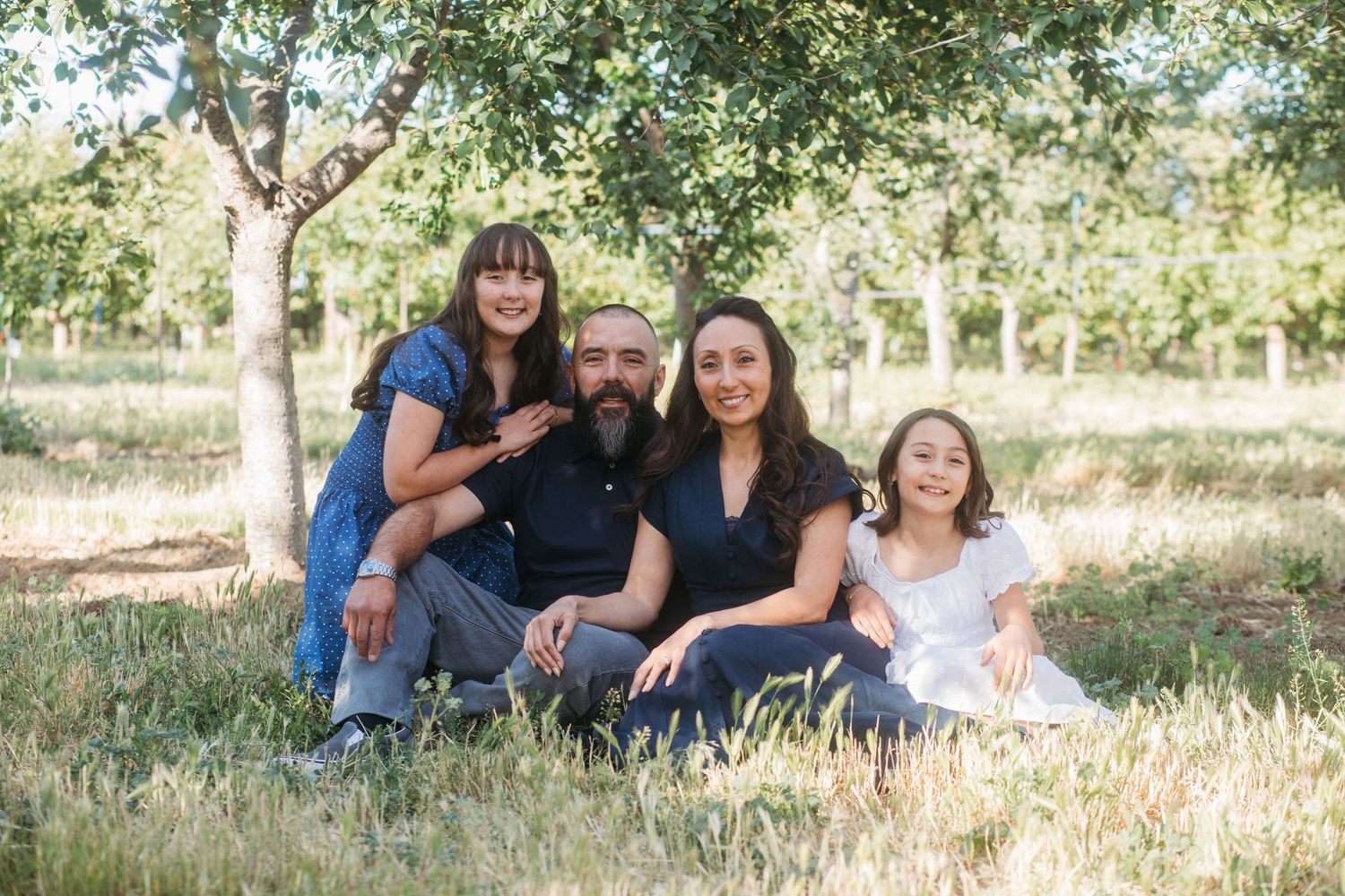 Family sitting together under orchard trees during a late spring family photo session in Boise.
