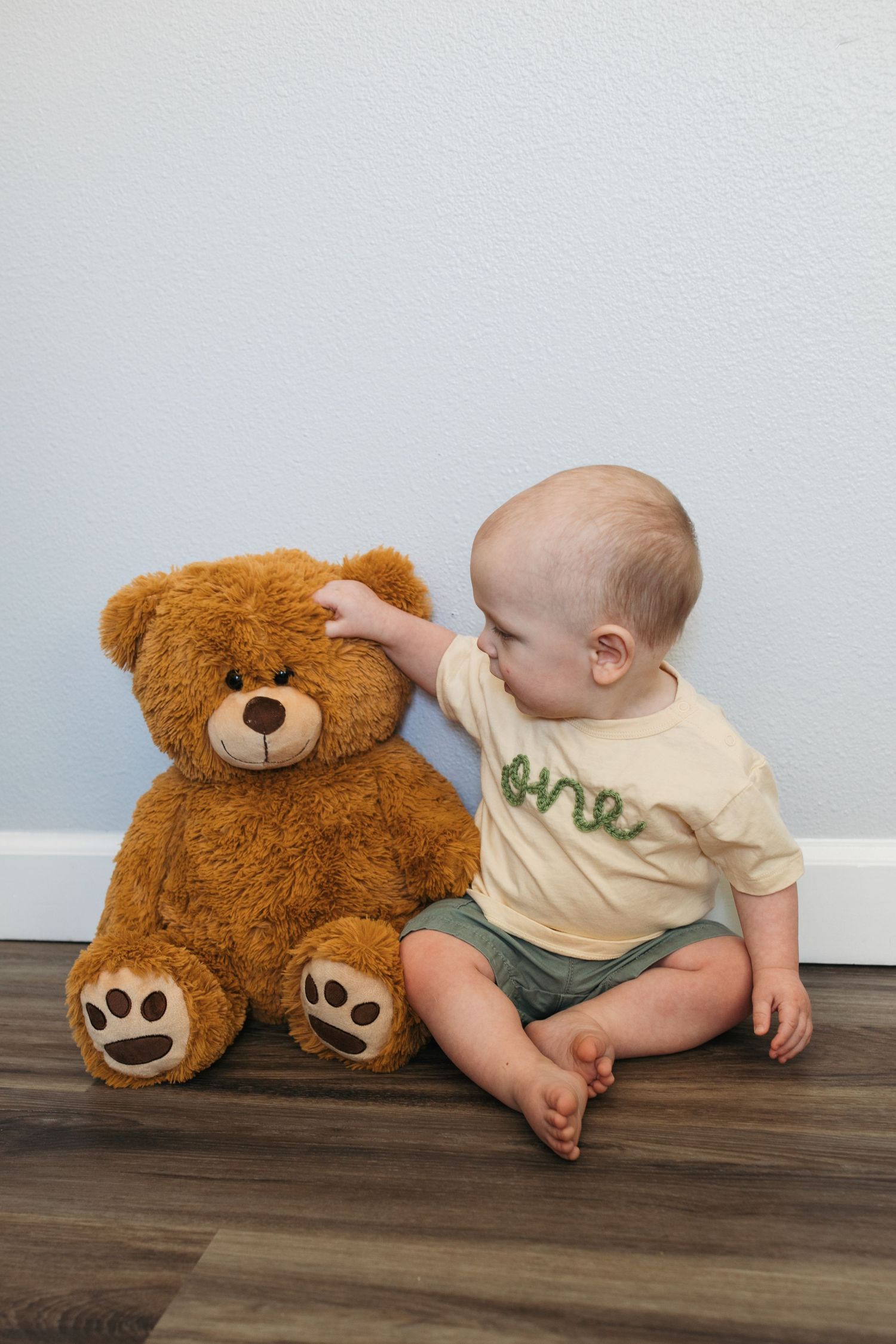 One year old boy sitting beside a teddy bear during a twin first birthday milestone session in Kuna, Idaho.