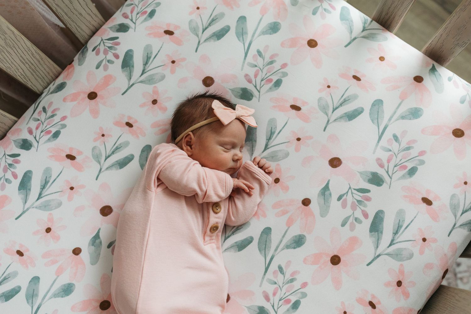 Newborn baby girl sleeping in her crib on a floral mattress during an in-home lifestyle newborn session in Middleton, Idaho.