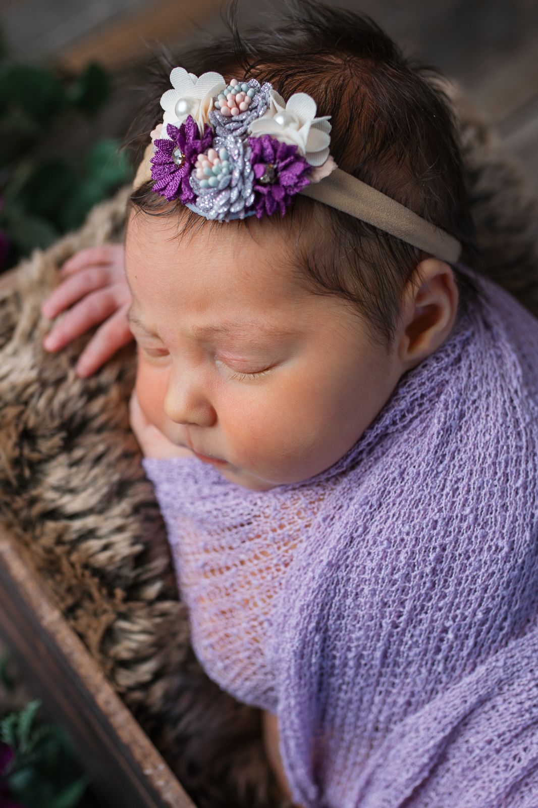 A sleeping newborn wrapped in a lavender knit blanket wearing delicate purple and white floral headpiece.  studio newborn photography