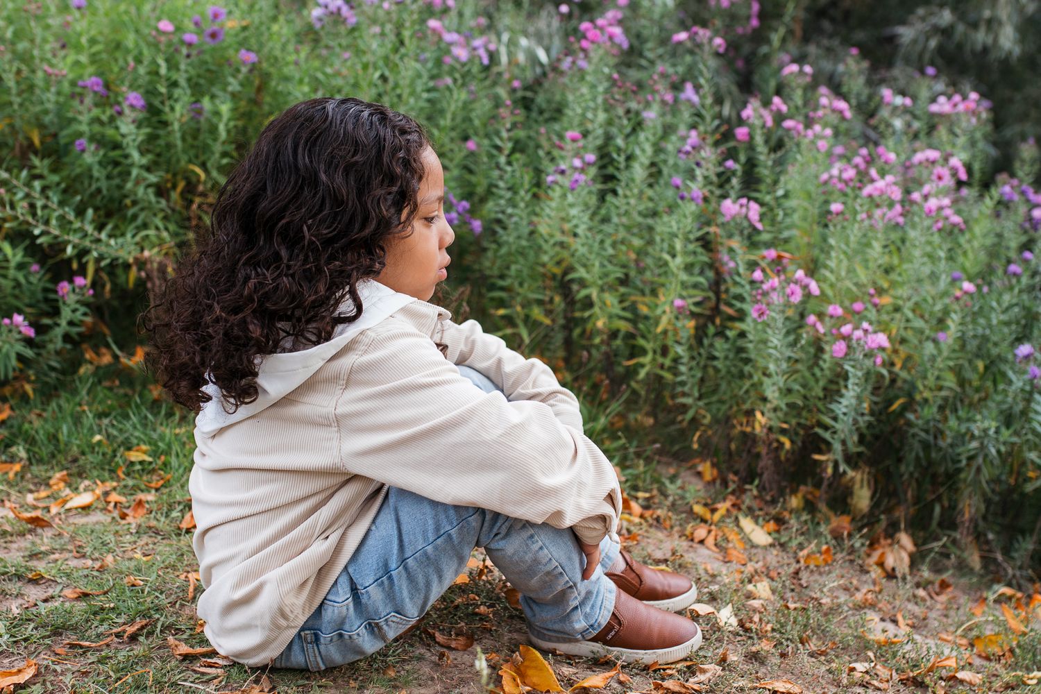 Someone in a beige hoodie and jeans sits by a garden of purple flowers on an autumn day birthday milestone photos Nampa Idaho