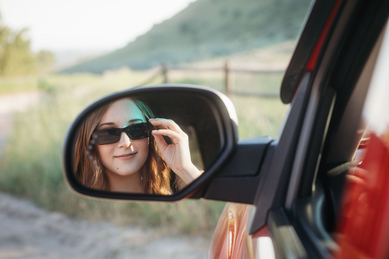 Boise senior photos of high school girl wearing sunglasses reflected in red truck side mirror during outdoor session