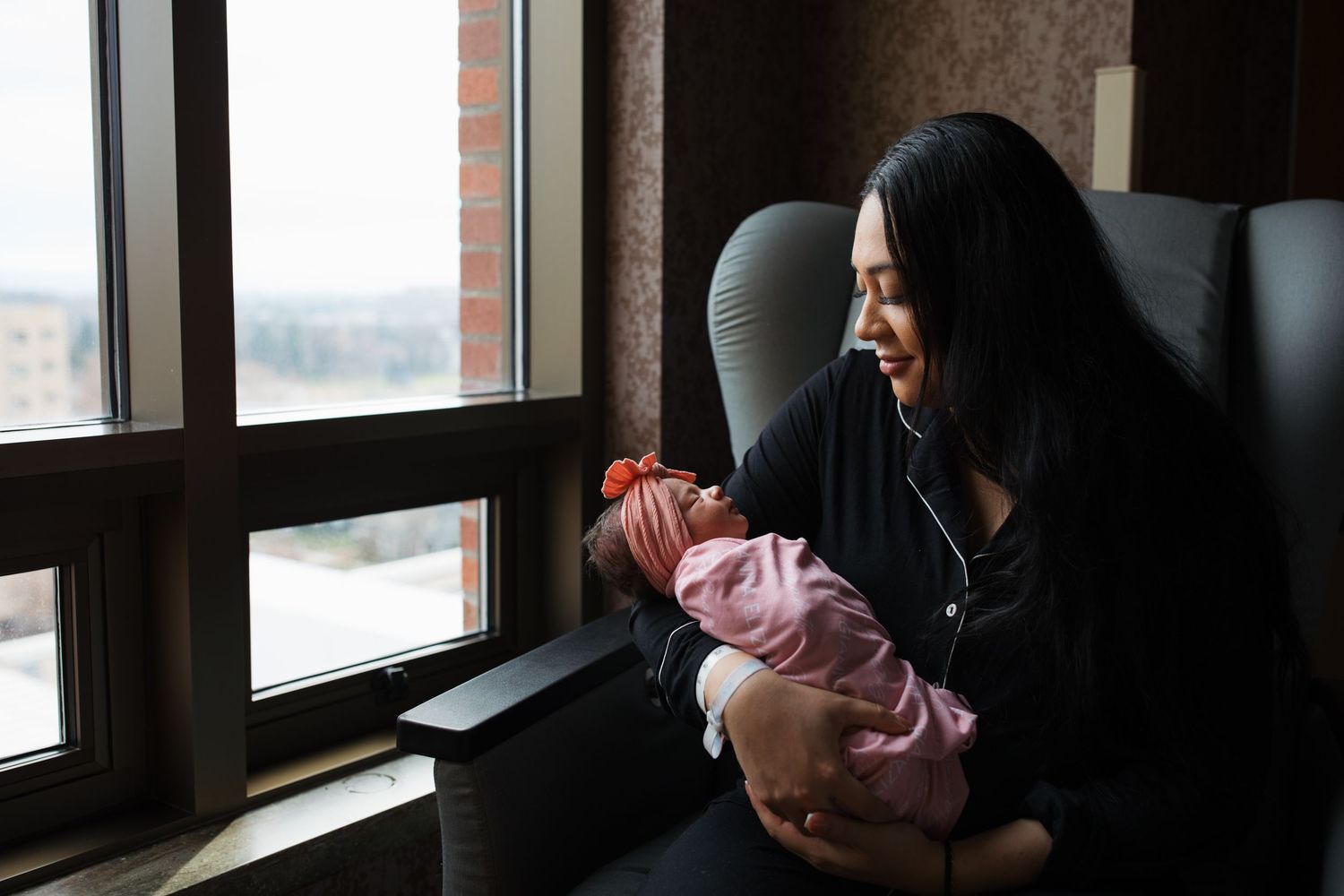 Mother holding her newborn near the hospital window during a calm Fresh 48 photography session