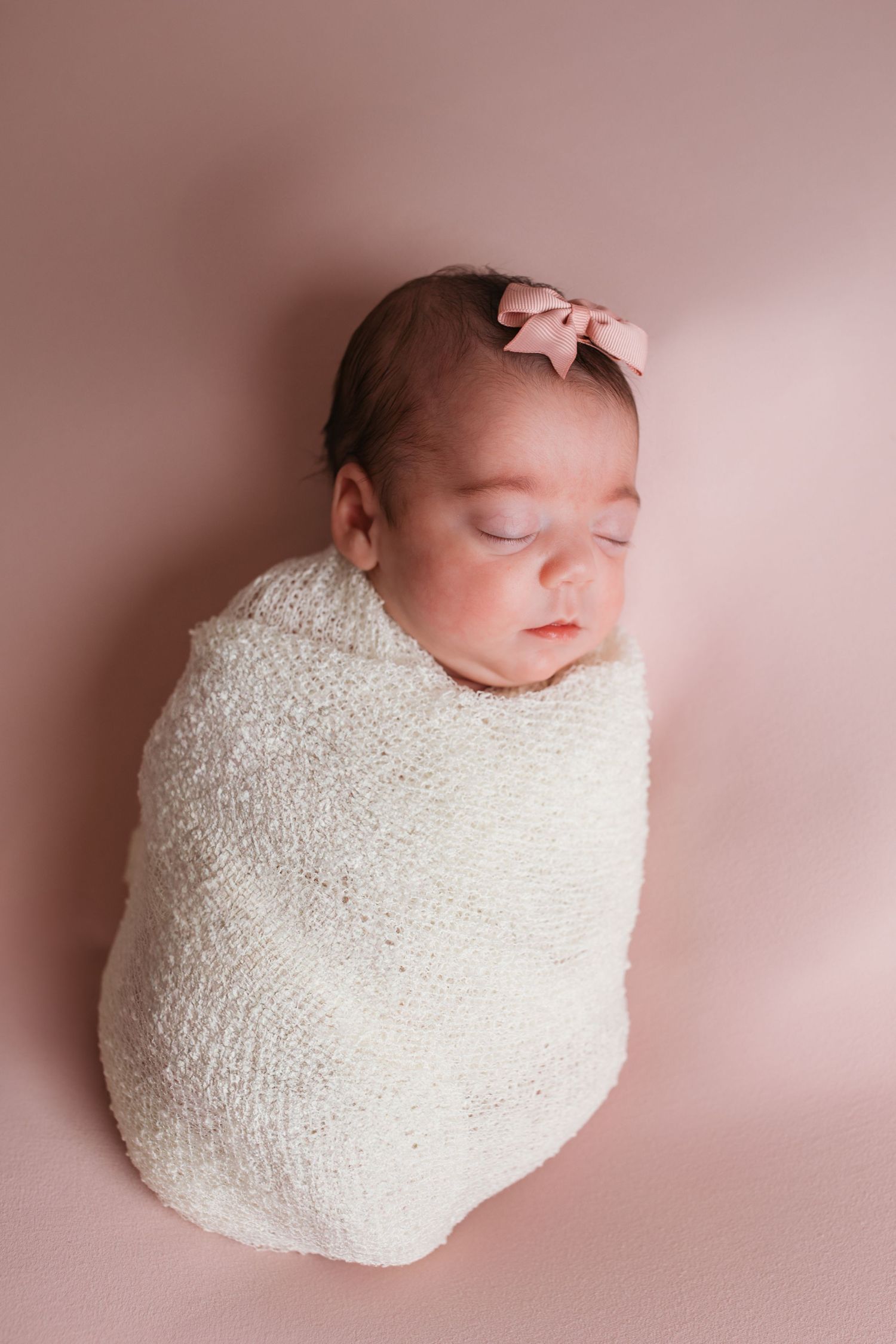 Newborn baby girl wrapped in cream on a soft pink backdrop in a Nampa photography studio