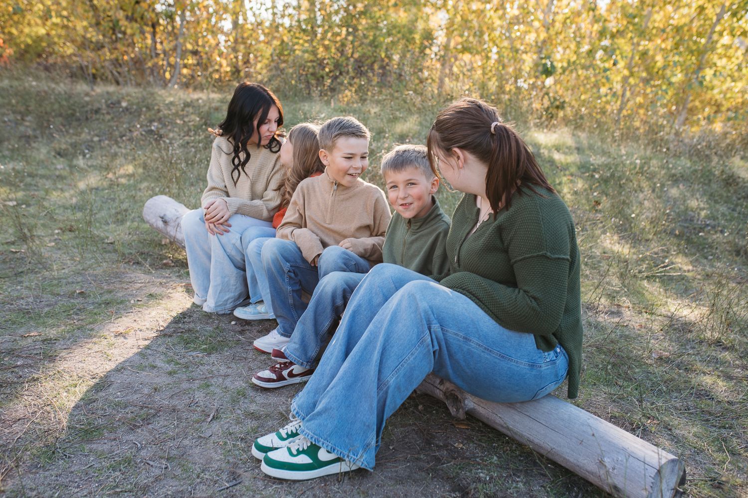 A group sits together outdoors on a log bench during autumn, sharing a casual moment in nature. Boise foothills family photography