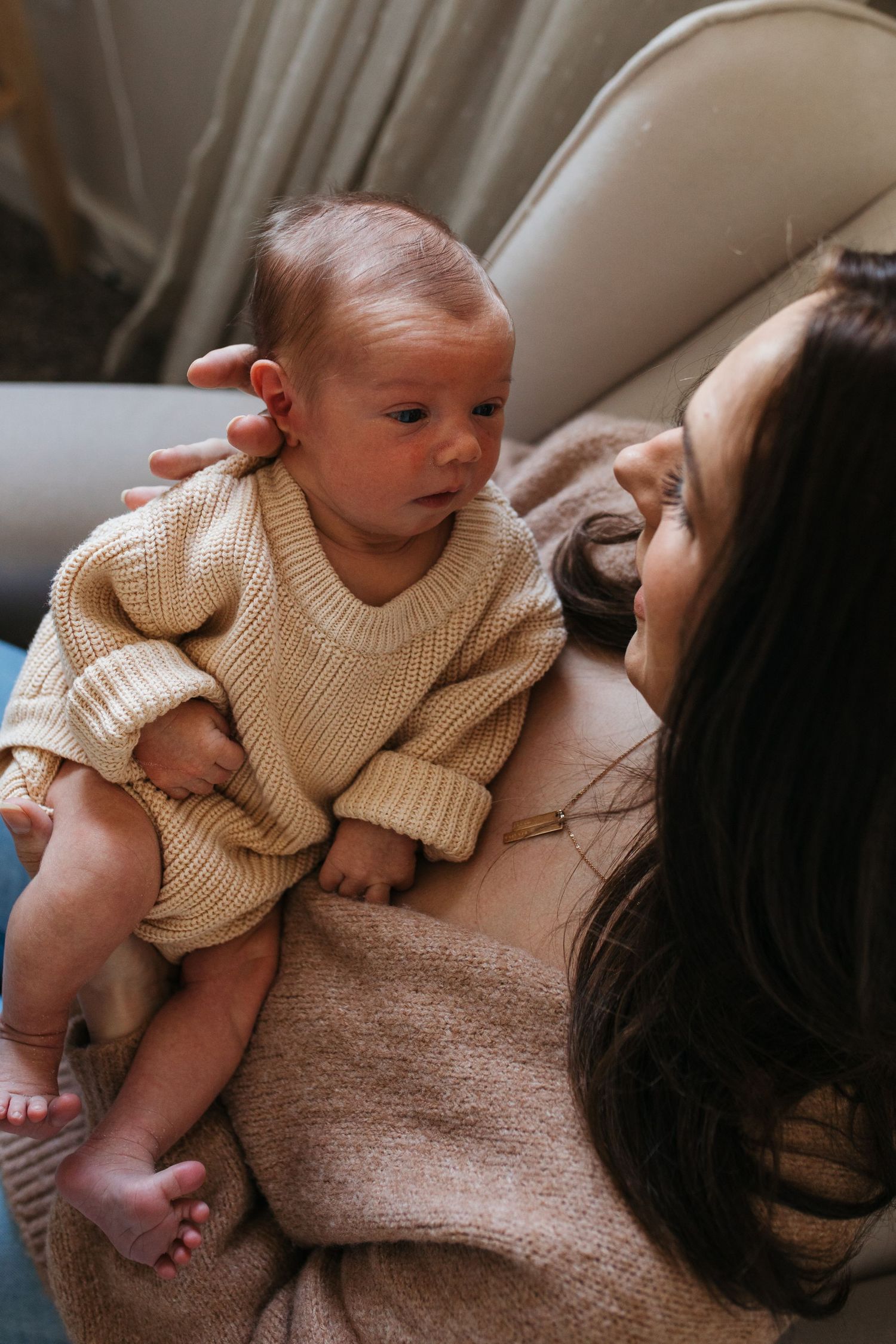 A baby in a beige sweater lies on someone's lap in a series of candid moments showing different angles and expressions - lifestyle in-home