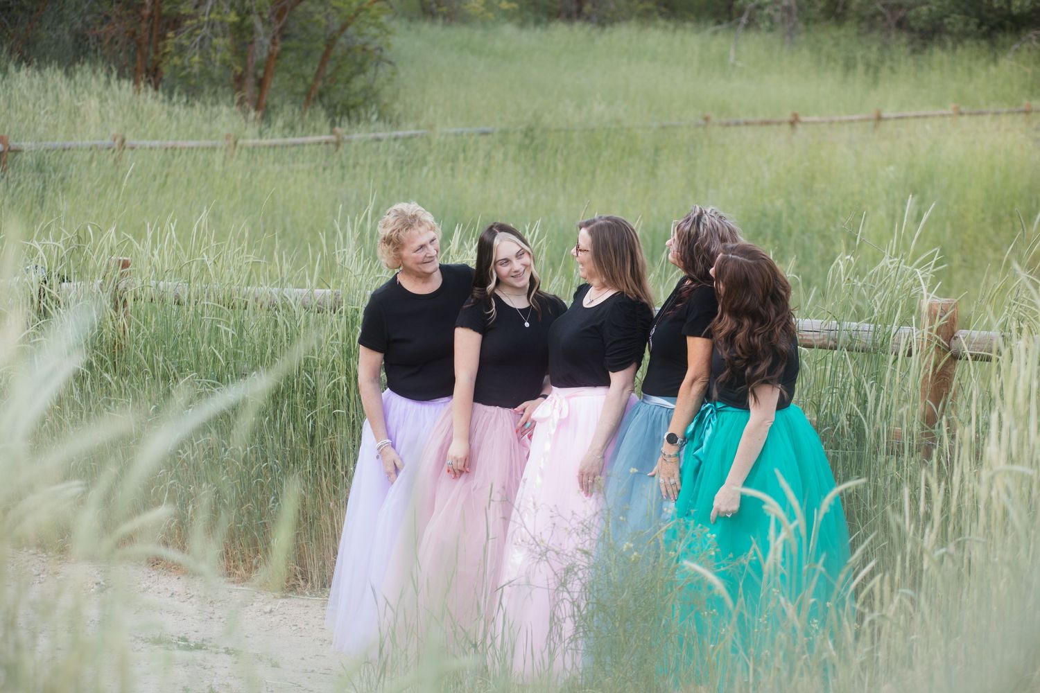 Four sisters laughing together in tall grass during a summer family photography session in the Treasure Valley, Idaho.