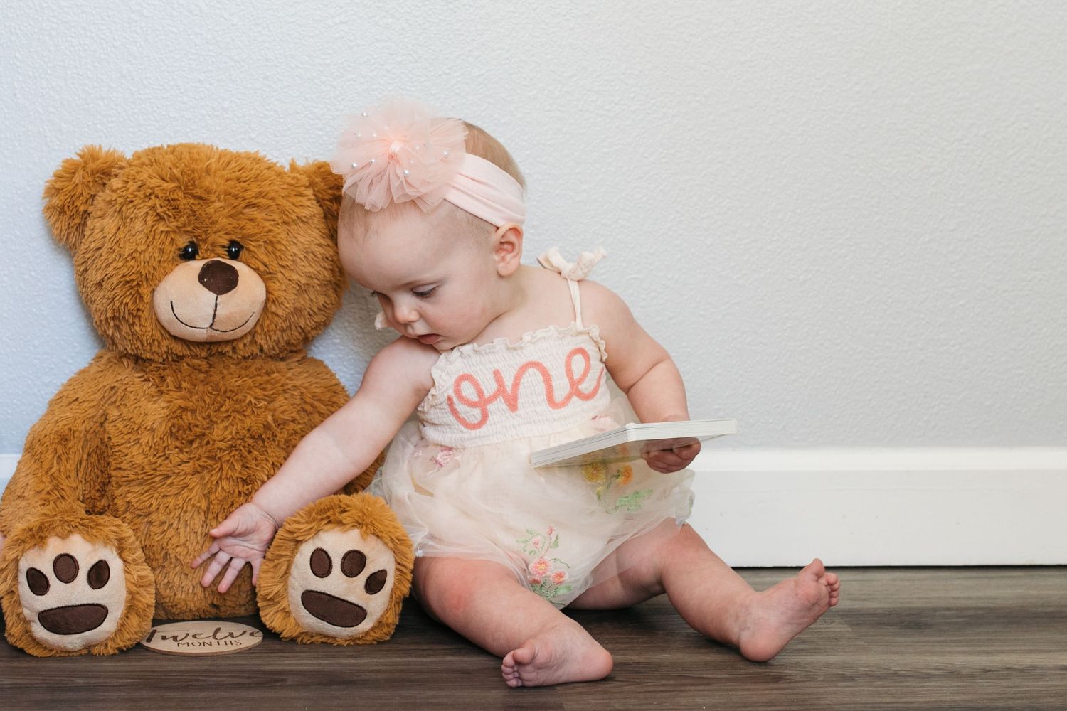 One year old girl sitting beside a teddy bear during a twin first birthday milestone session in Kuna, Idaho.