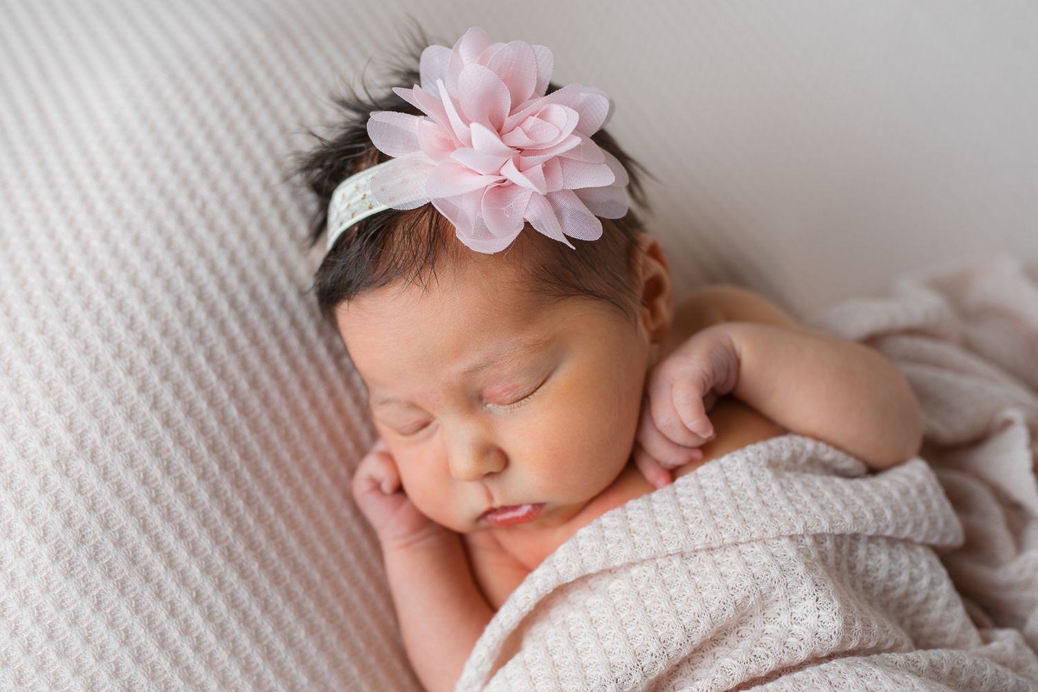 A sleeping newborn baby wearing a pink floral headband lies peacefully swaddled in soft white fabric  studio newborn photography Caldwell ID