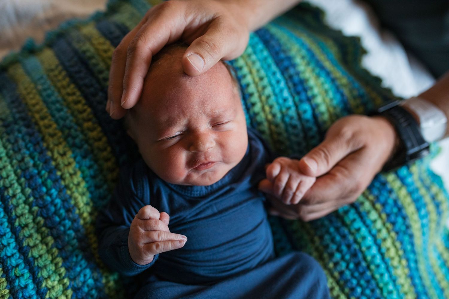 Hands holding a small baby wrapped in a blue and green crocheted blanket- Fresh 48 session in hospital Boise, Idaho