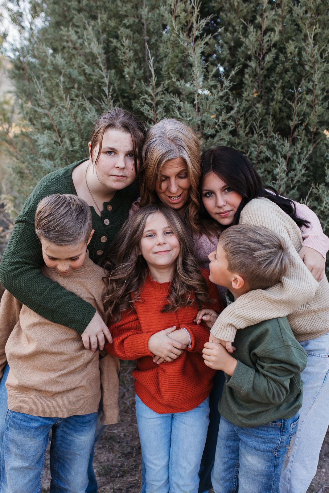 A family hugging and laughing together in casual fall outfits against an evergreen backdrop. Boise foothills family photography