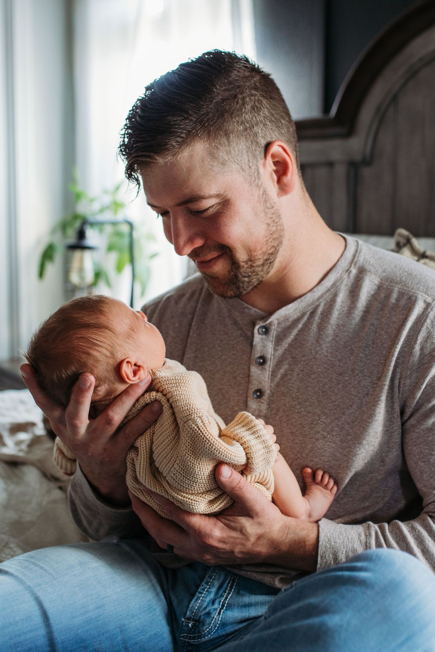 A tender moment between dad and newborn baby  against soft window light - lifestyle in-home newborn photos Boise