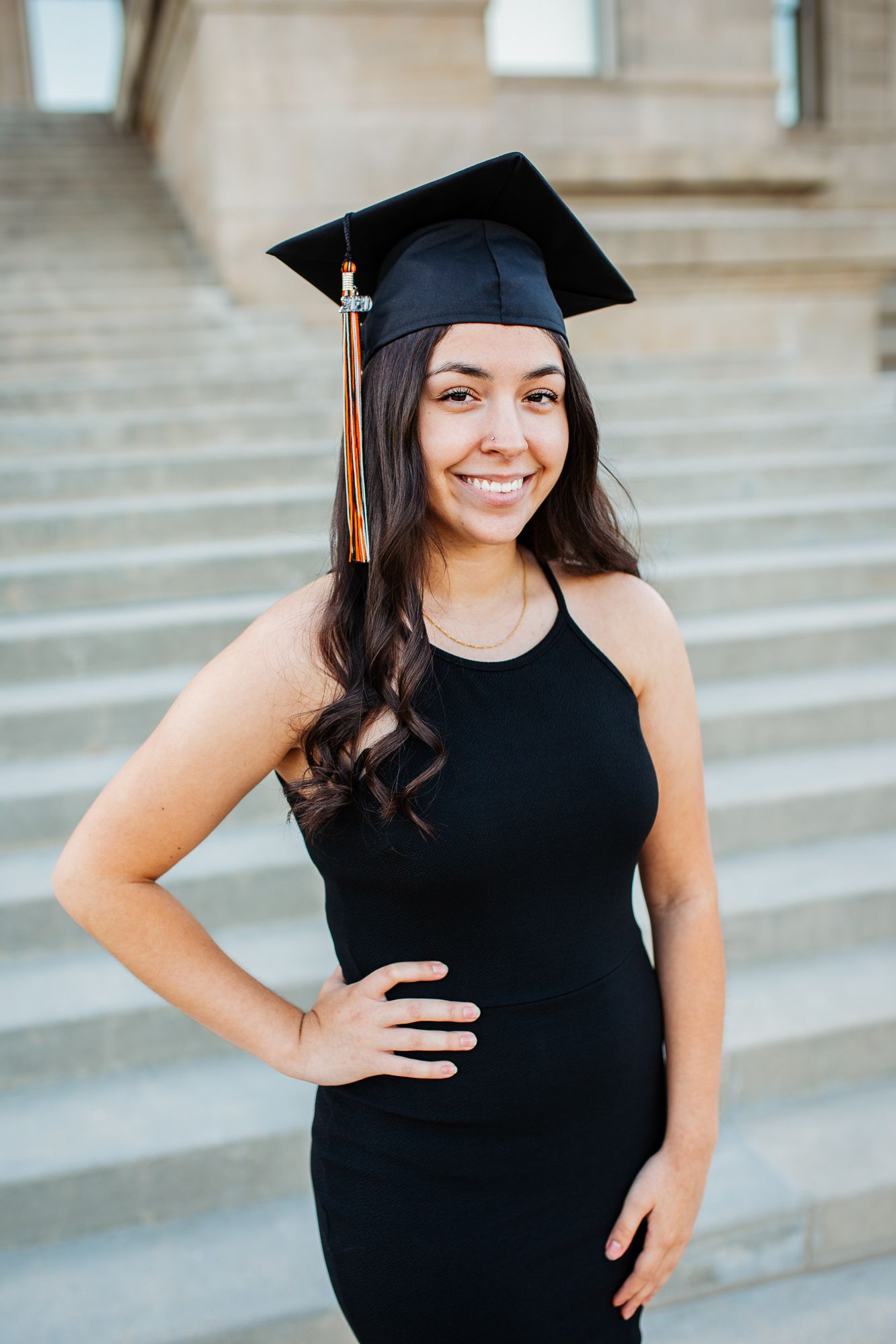 Graduate in black cap and gown poses on stone steps during graduation photo session - Senior photos Boise Idaho