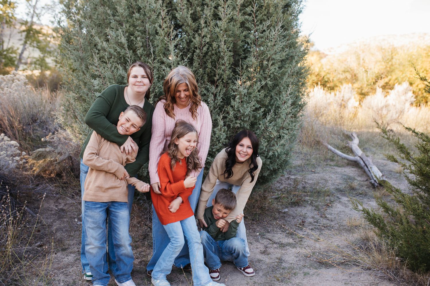 A group of people pose together outdoors near evergreen trees during a golden sunset photoshoot. Boise foothills family photography
