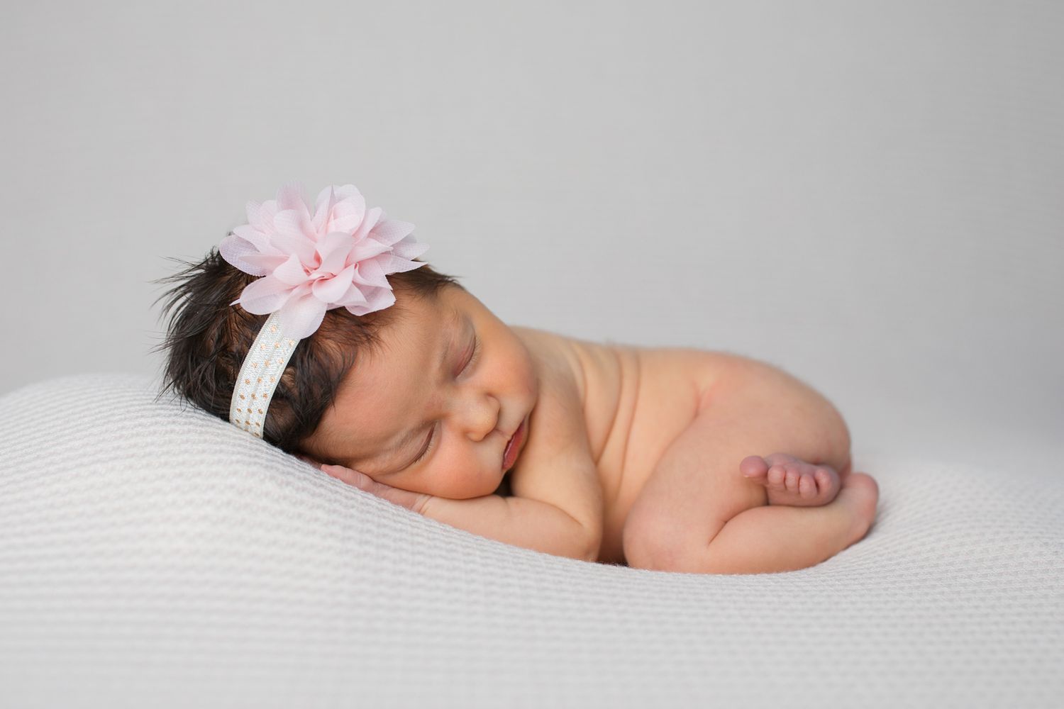 A sleeping newborn baby wearing a pink bow headband rests peacefully on white fabric studio newborn photography Caldwell Idaho