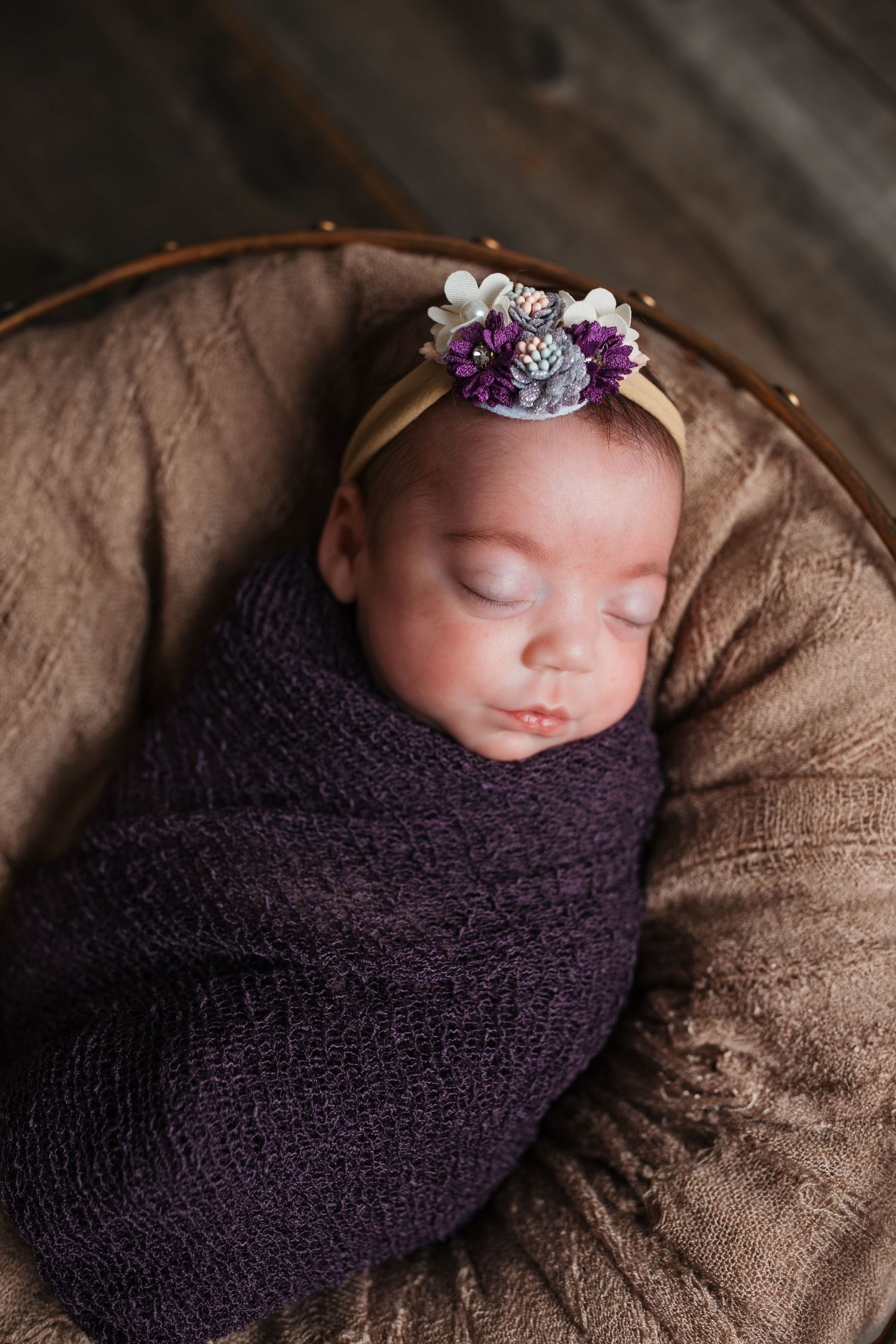 Sleeping newborn baby girl wrapped in purple with a floral headband during a studio newborn session in Nampa, Idaho