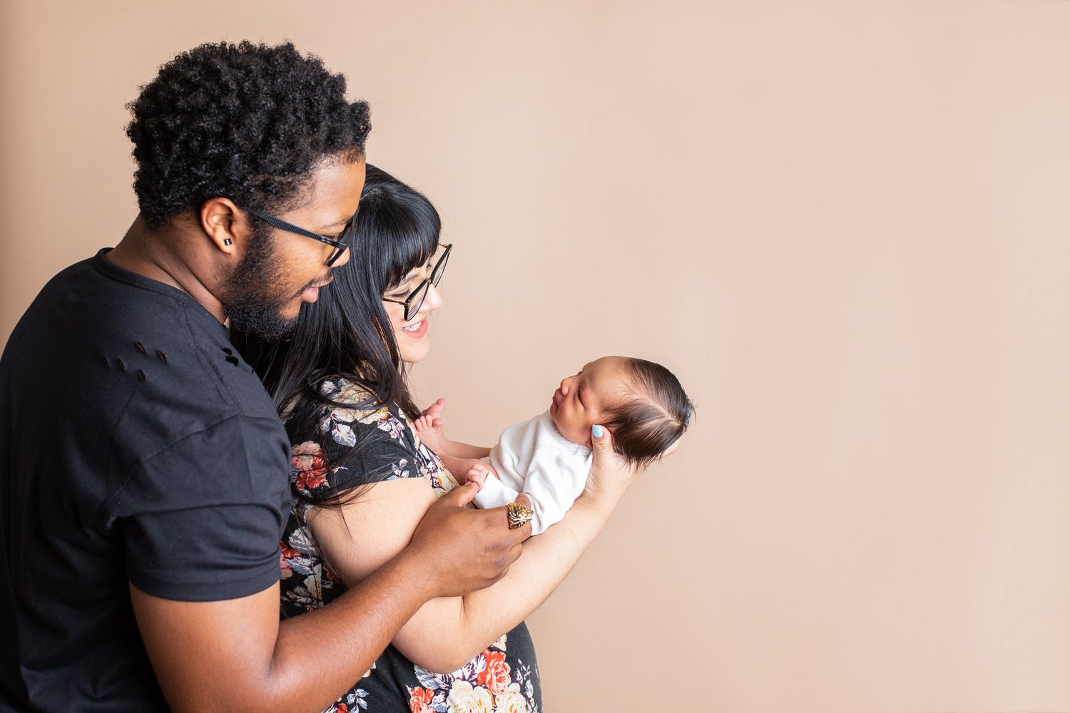 A couple holding and gazing lovingly at their newborn baby against a neutral beige wall -studio newborn photography Nampa Idaho