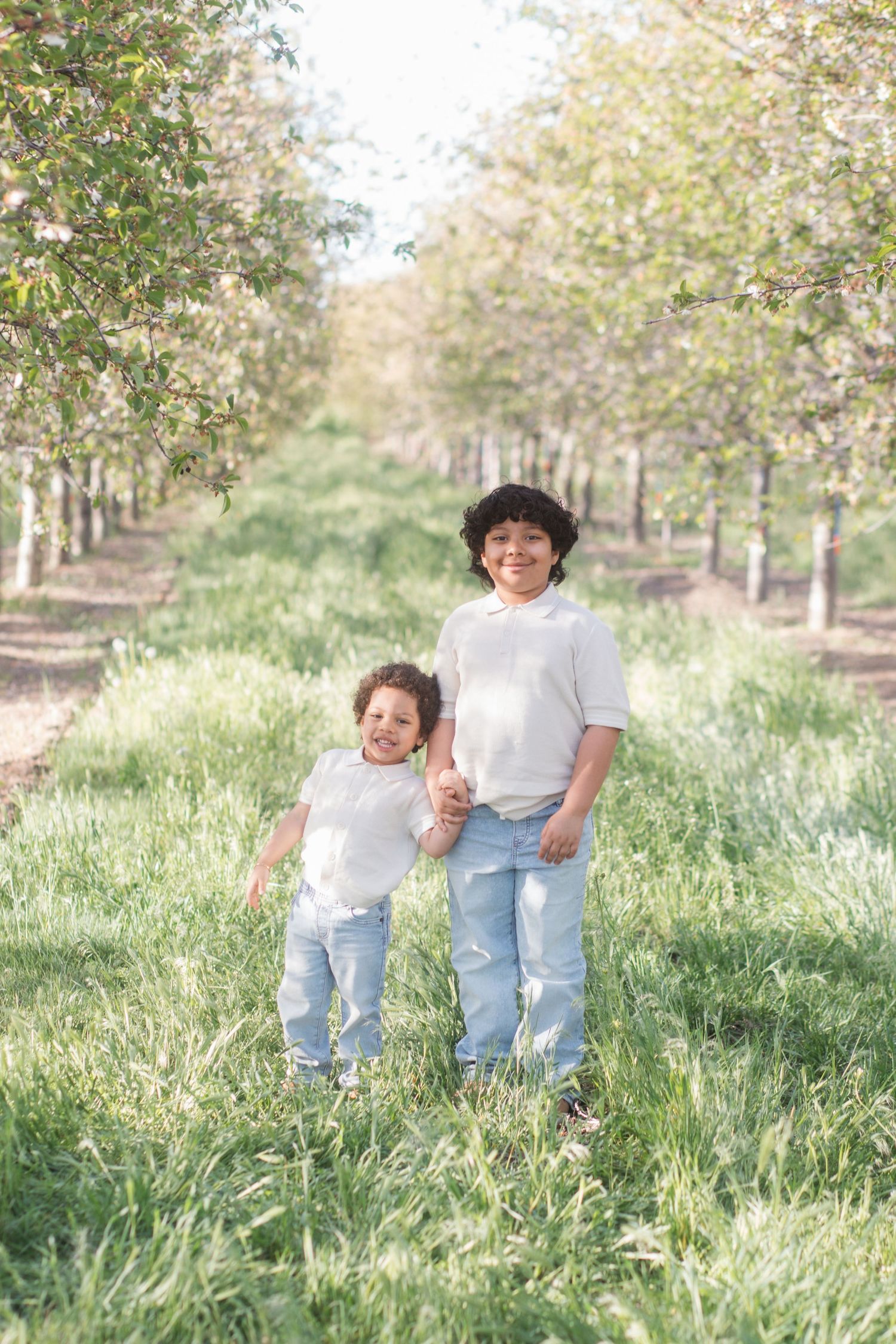 Brothers walking hand in hand through cherry blossom orchard at Cherry Hill Farms in Caldwell Idaho