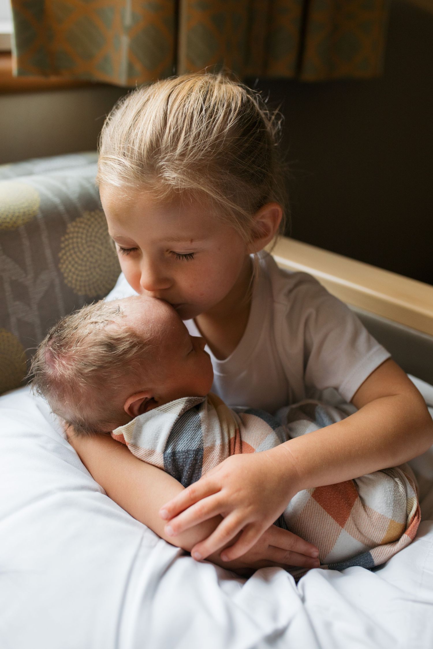 Two siblings share a tender moment as the older child gently kisses the new baby. Boise Fresh 48 session by Sara Elizabeth Photography
