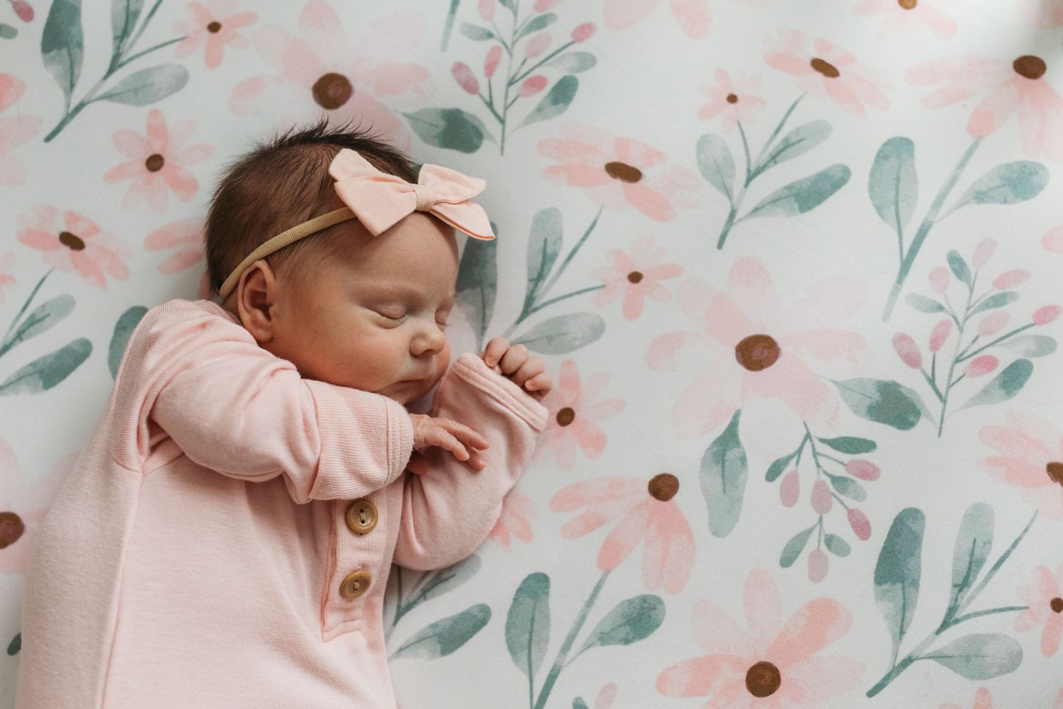 Newborn baby girl sleeping on a floral crib sheet in Middleton, Idaho, wearing a pink bow during her lifestyle newborn session.