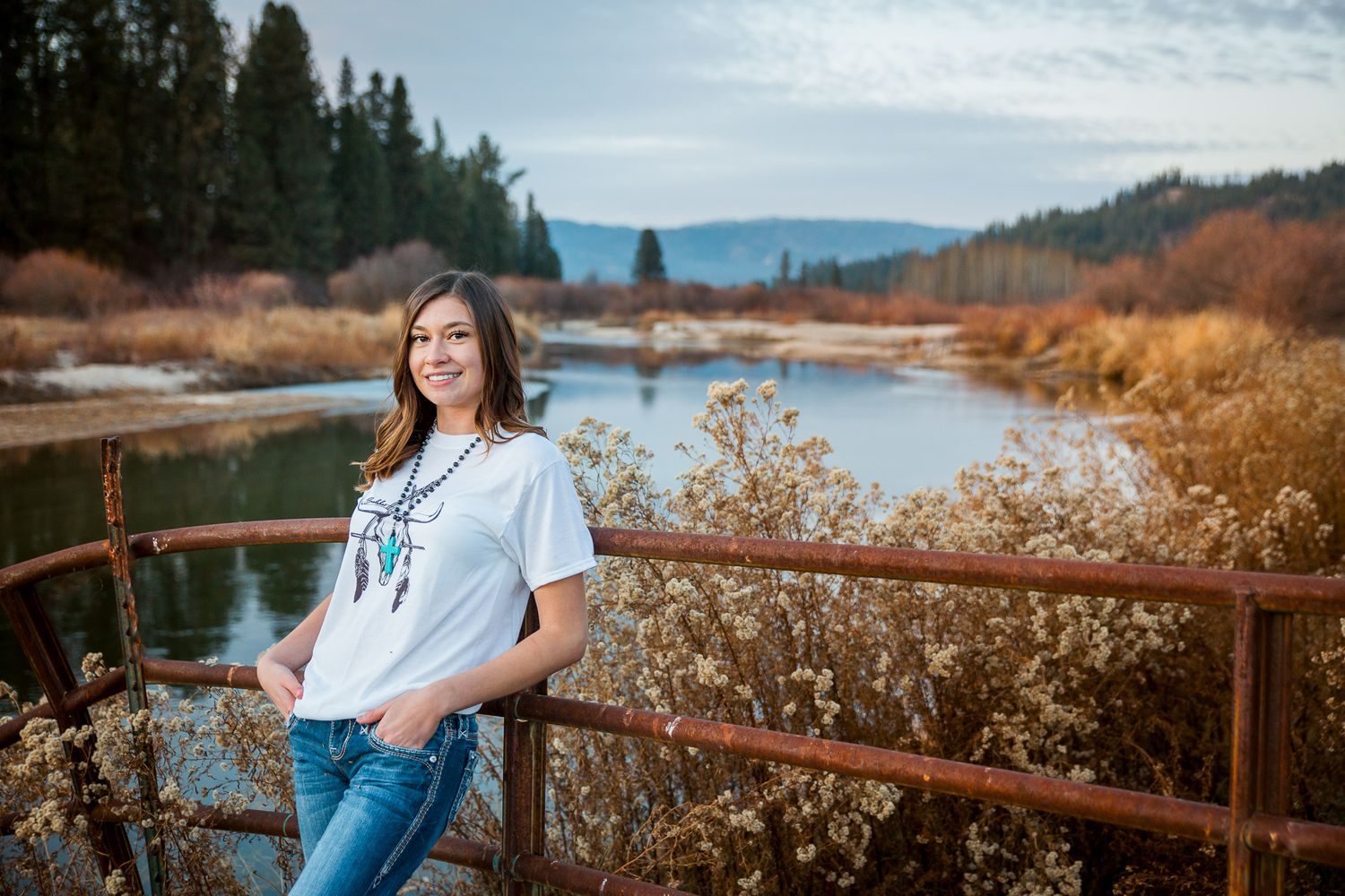 Person in casual attire poses against rustic wooden railing with scenic mountain lake views in autumn landscape - Senior photos Boise Idaho