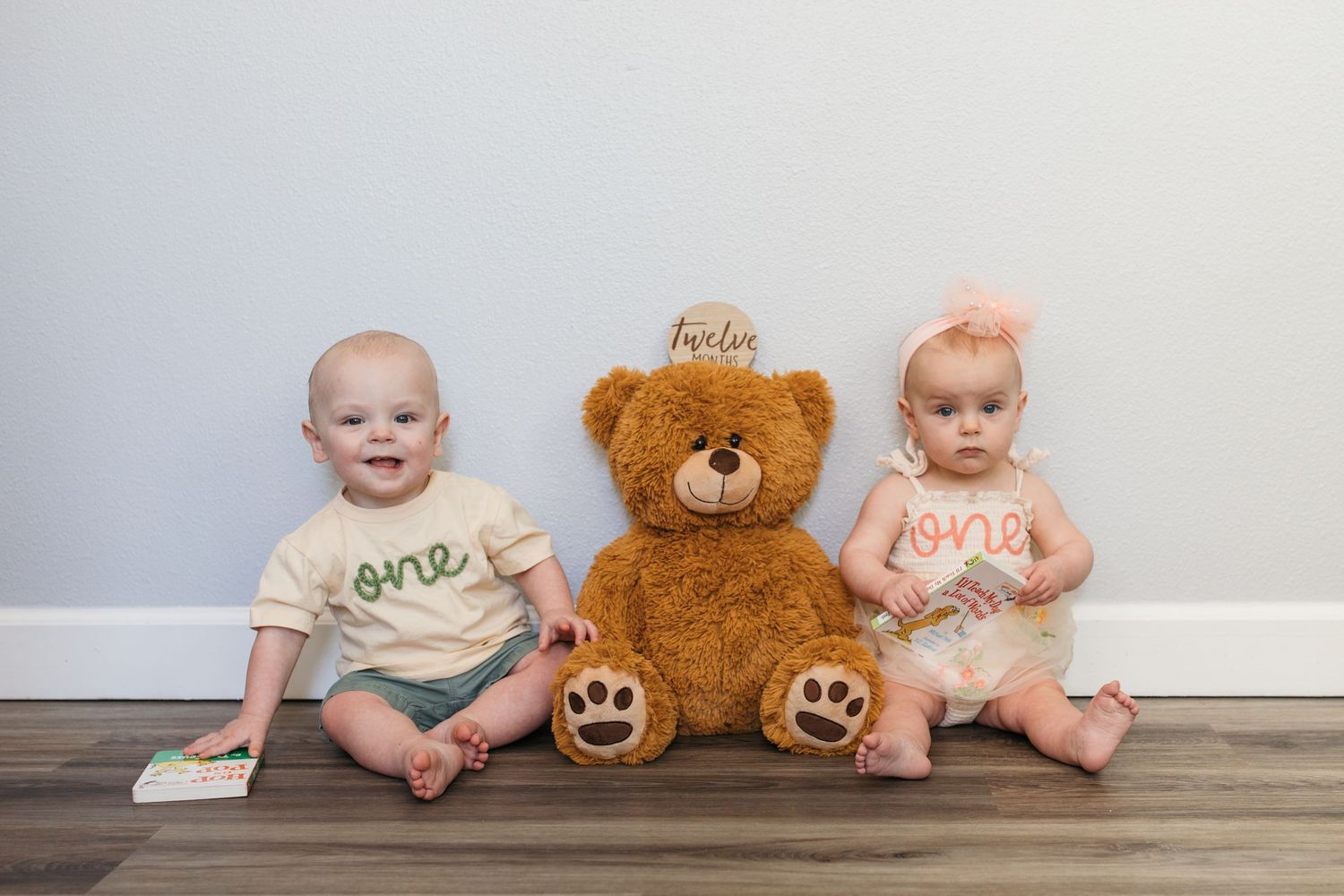 Twin one year old milestone portrait in Kuna Idaho featuring siblings sitting with a teddy bear during a first birthday session.