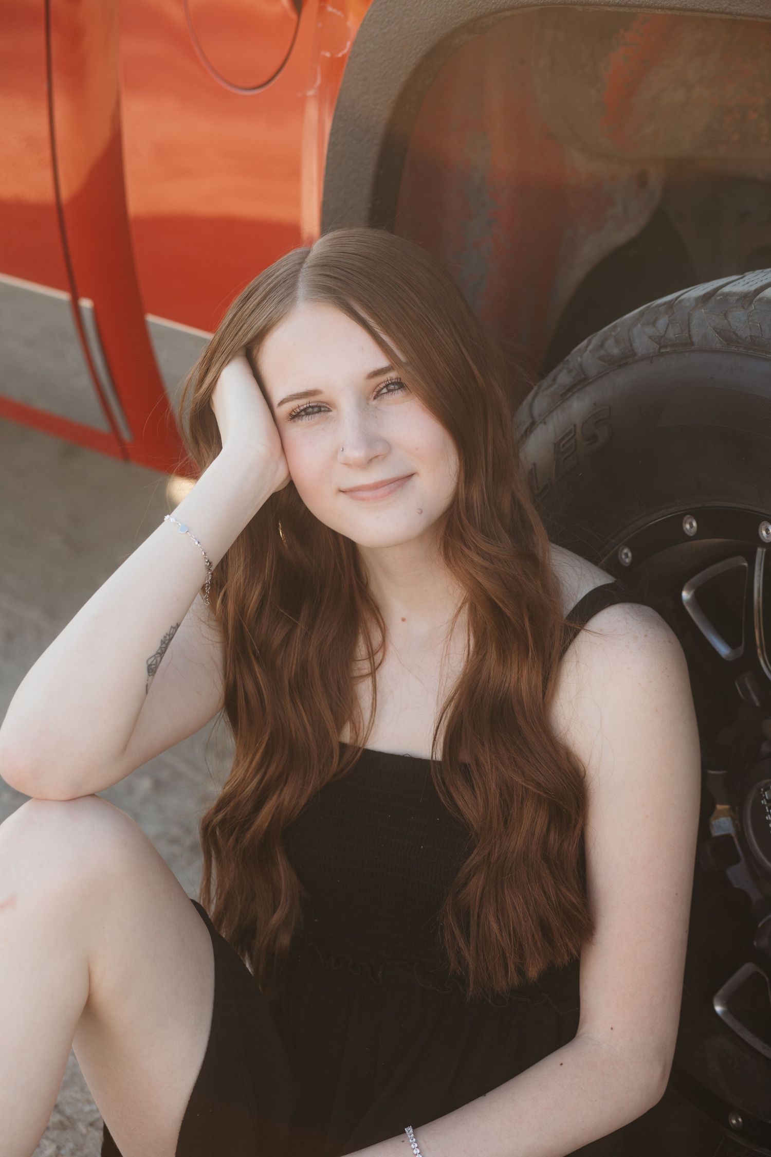 Boise senior photos of high school girl sitting by red truck tire in soft golden hour light during outdoor session