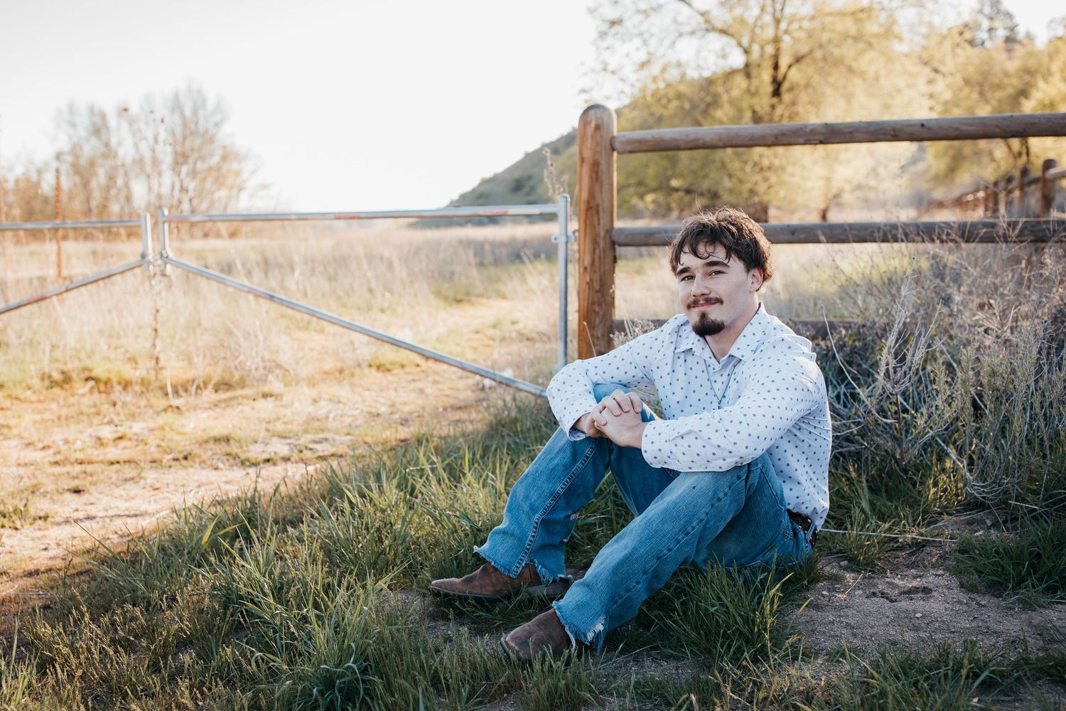 High school senior sitting in grass by wooden fence during outdoor Boise Idaho senior photo session