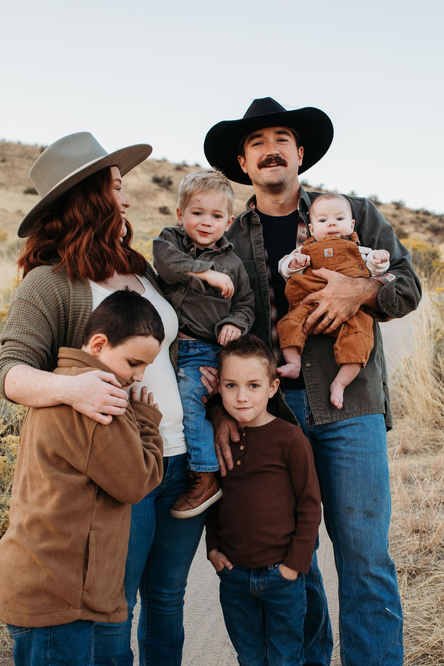 A family wearing western attire stands together in a desert landscape during golden hour - lifestyle family photos in Boise