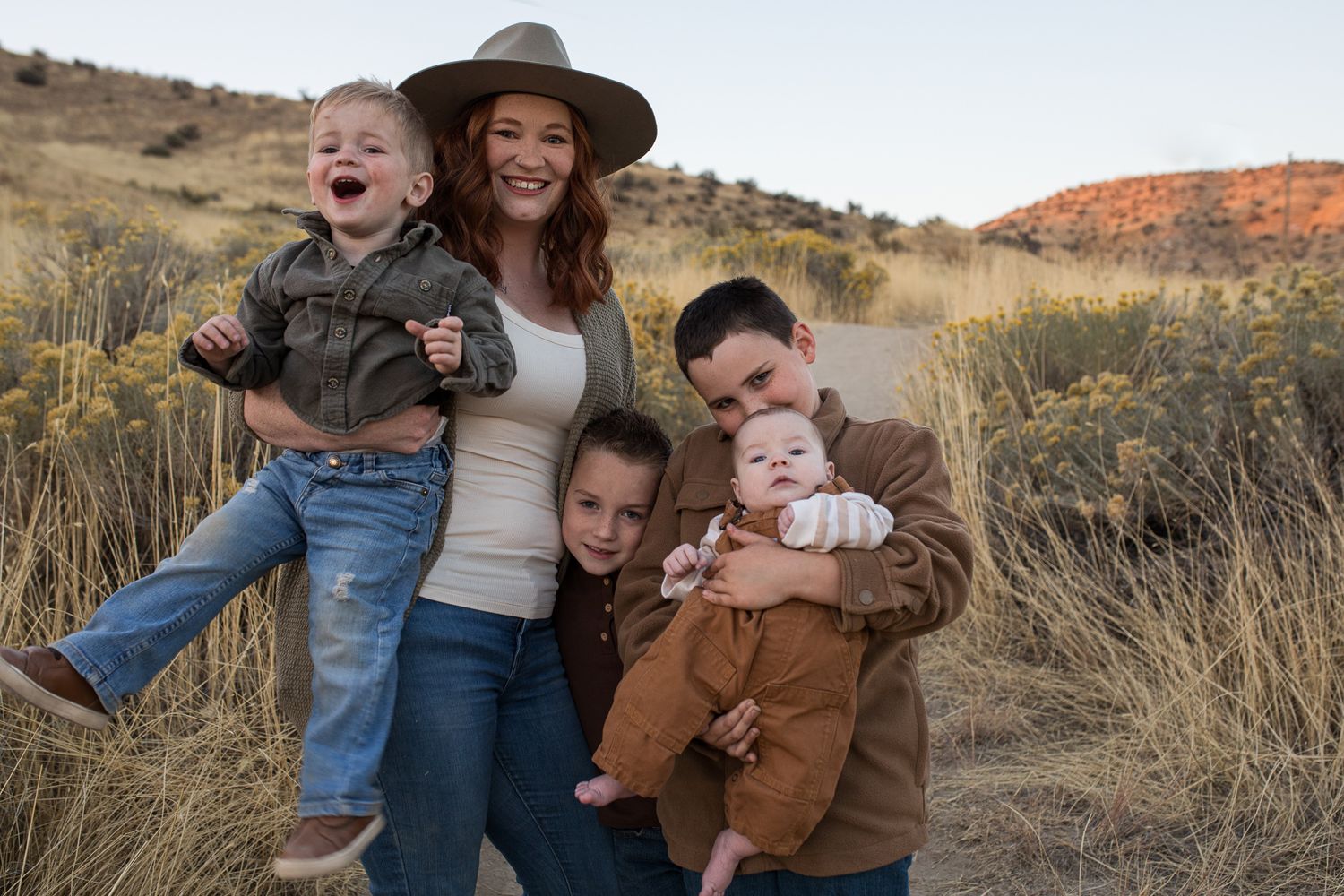 A family shares joyful moments together while posing in a desert landscape with golden grass and mountains- lifestyle family photos in Bois