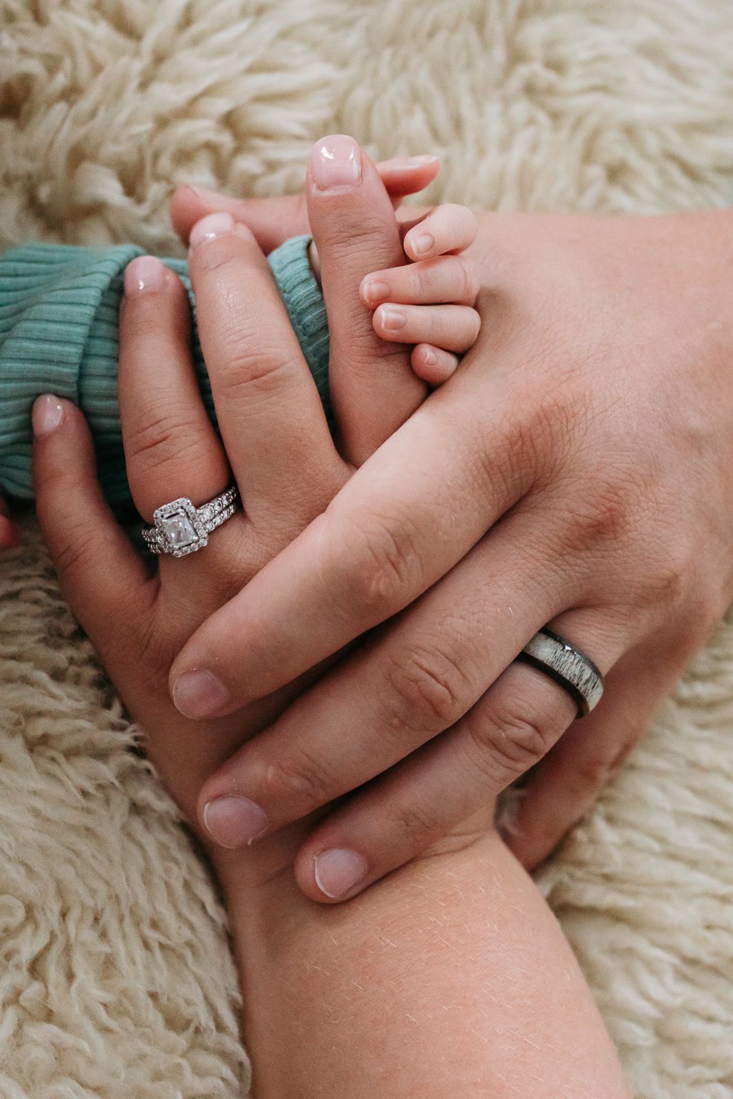 Close-up of parents hands wearing wedding rings holding newborn hand on a white fluffy rug - lifestyle in-home newborn photos Boise