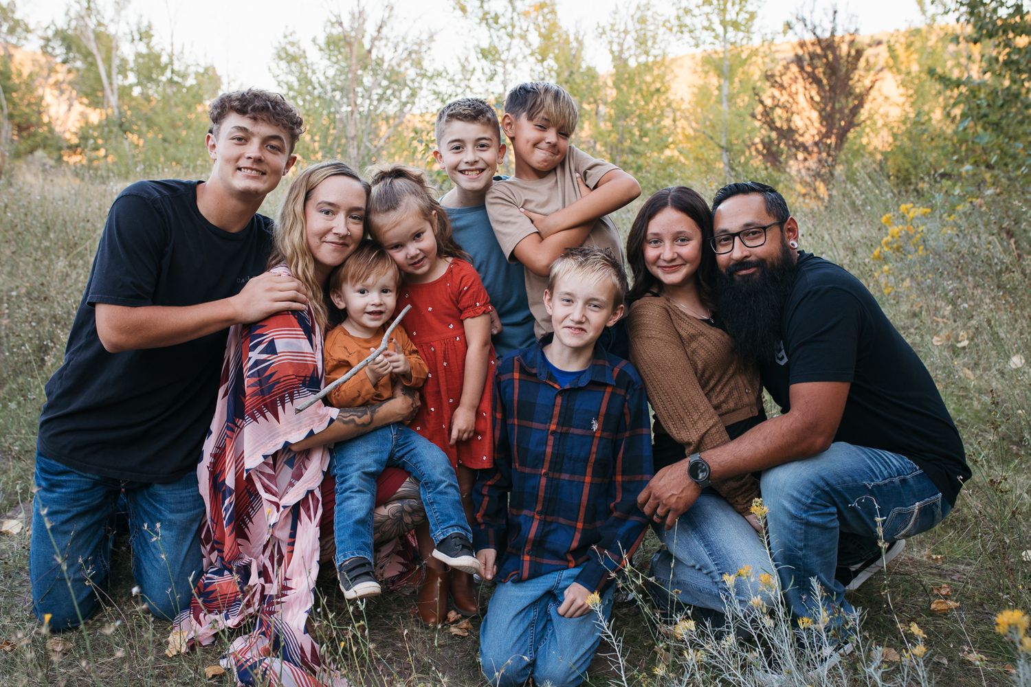 A large family poses together outdoors during golden hour in a natural setting with trees and grass - lifestyle family photography Boise