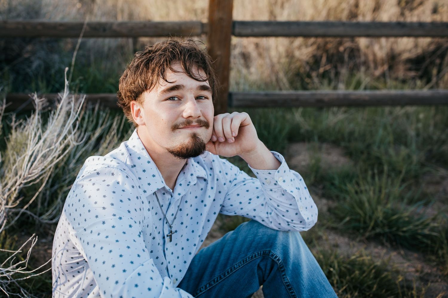 High school senior boy sitting by wooden fence during outdoor Boise Idaho senior photo session