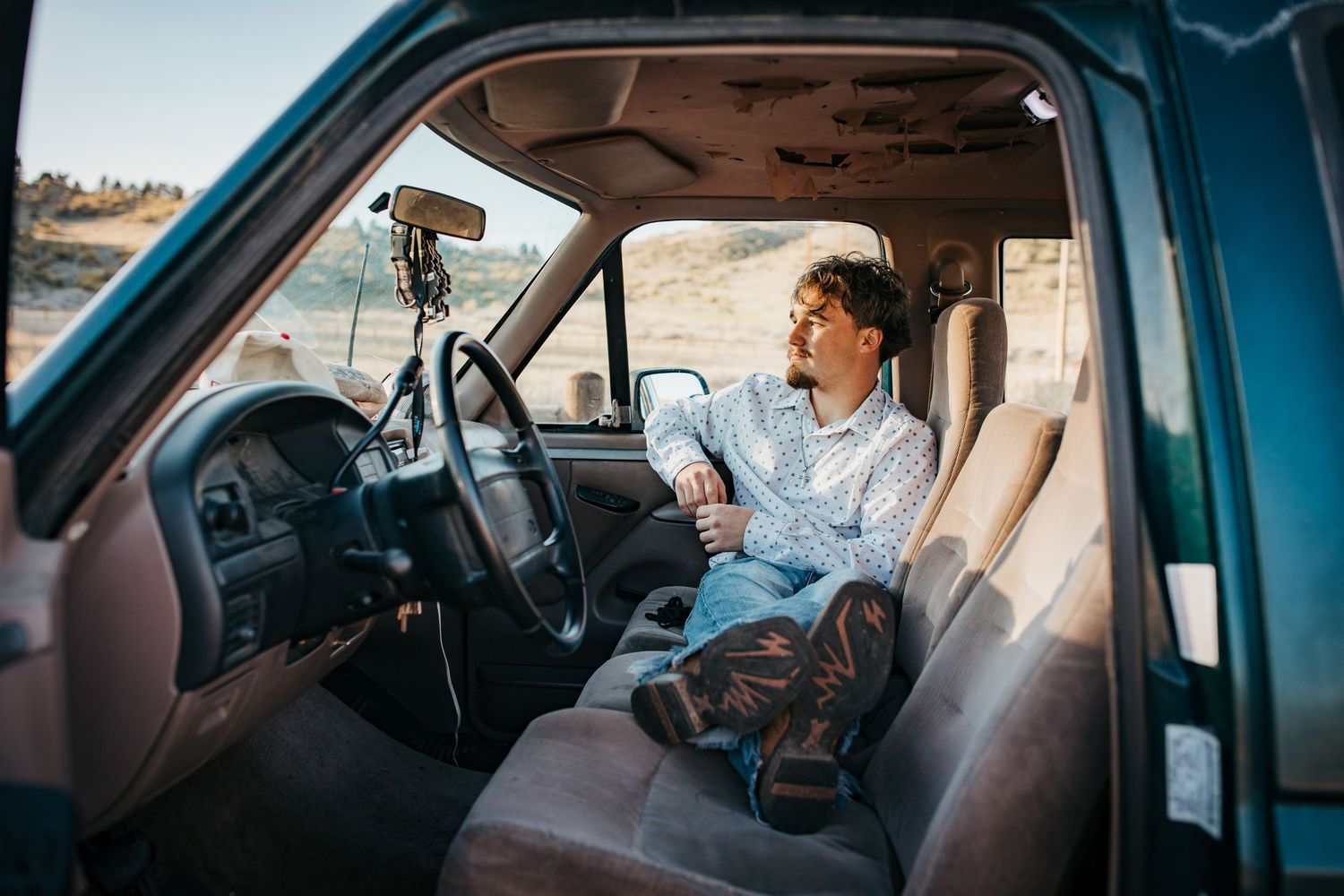 High school senior sitting in truck with feet up looking out window during Boise Idaho senior photo session