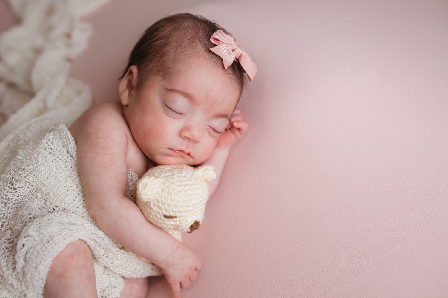 Newborn baby girl cuddling a small knit teddy bear during a studio newborn session in Nampa, Idaho