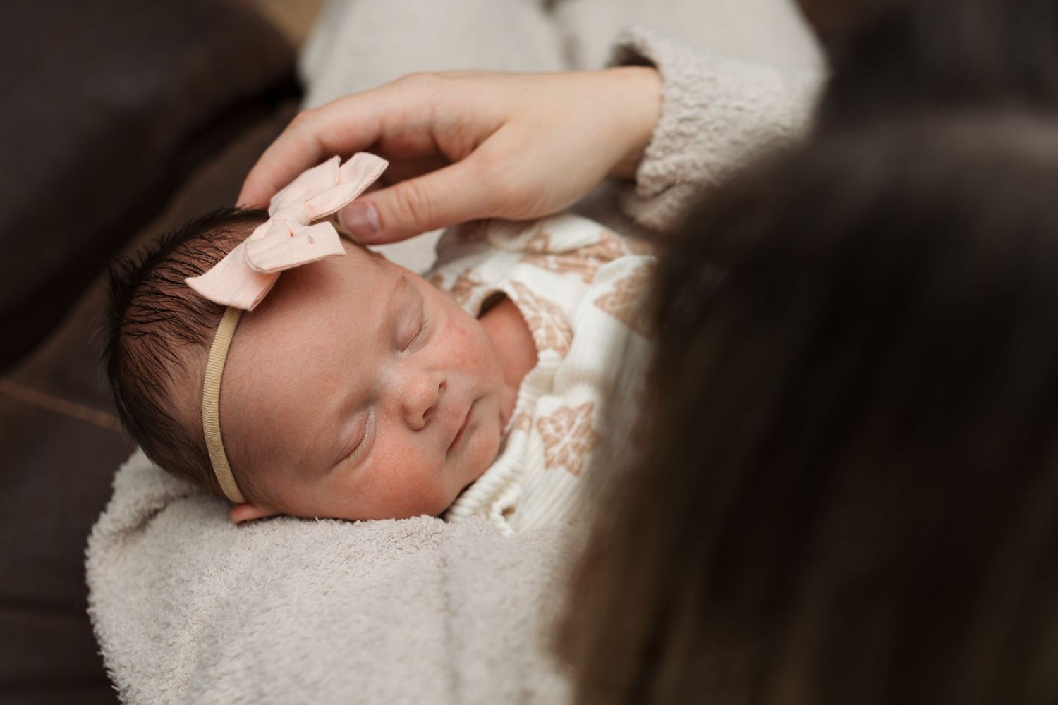 Close-up of a newborn sleeping while her mother gently adjusts her bow during a cozy in-home session in Middleton, Idaho.