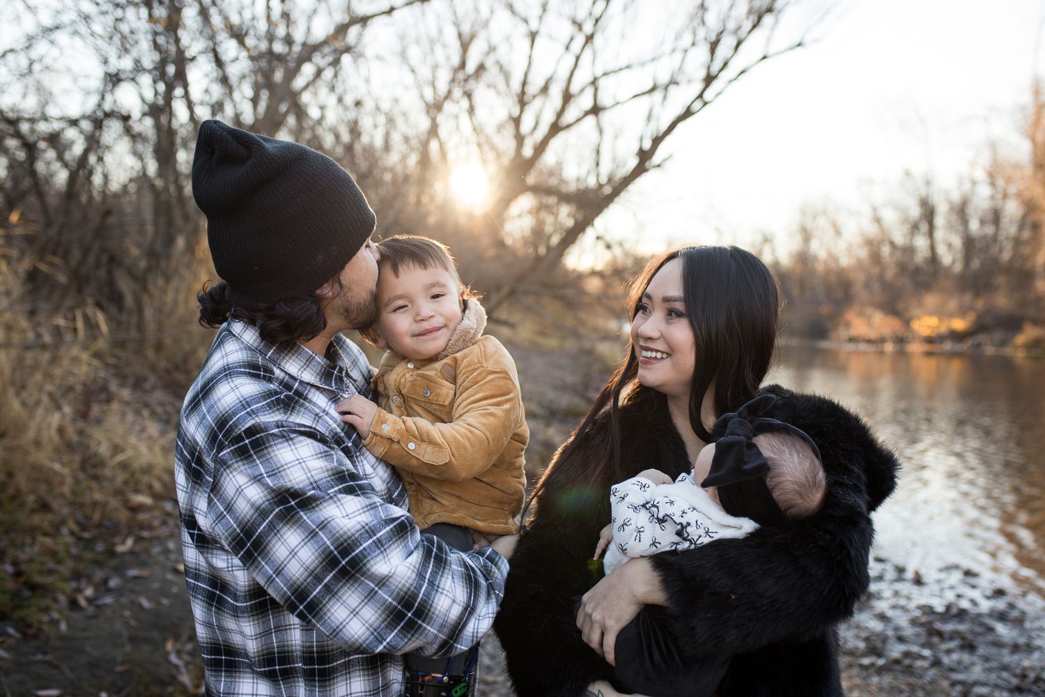 Family standing by the river at Reid Merrill Park in Eagle, Idaho during golden winter sunset, smiling and holding their children.