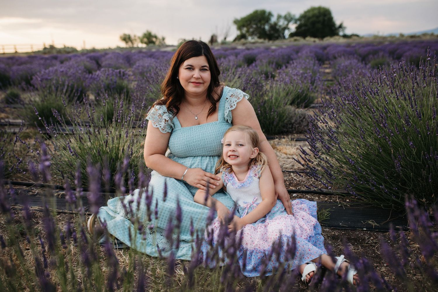 Mother and daughter sitting together in a blooming Idaho lavender field during a summer family photo session at sunset.