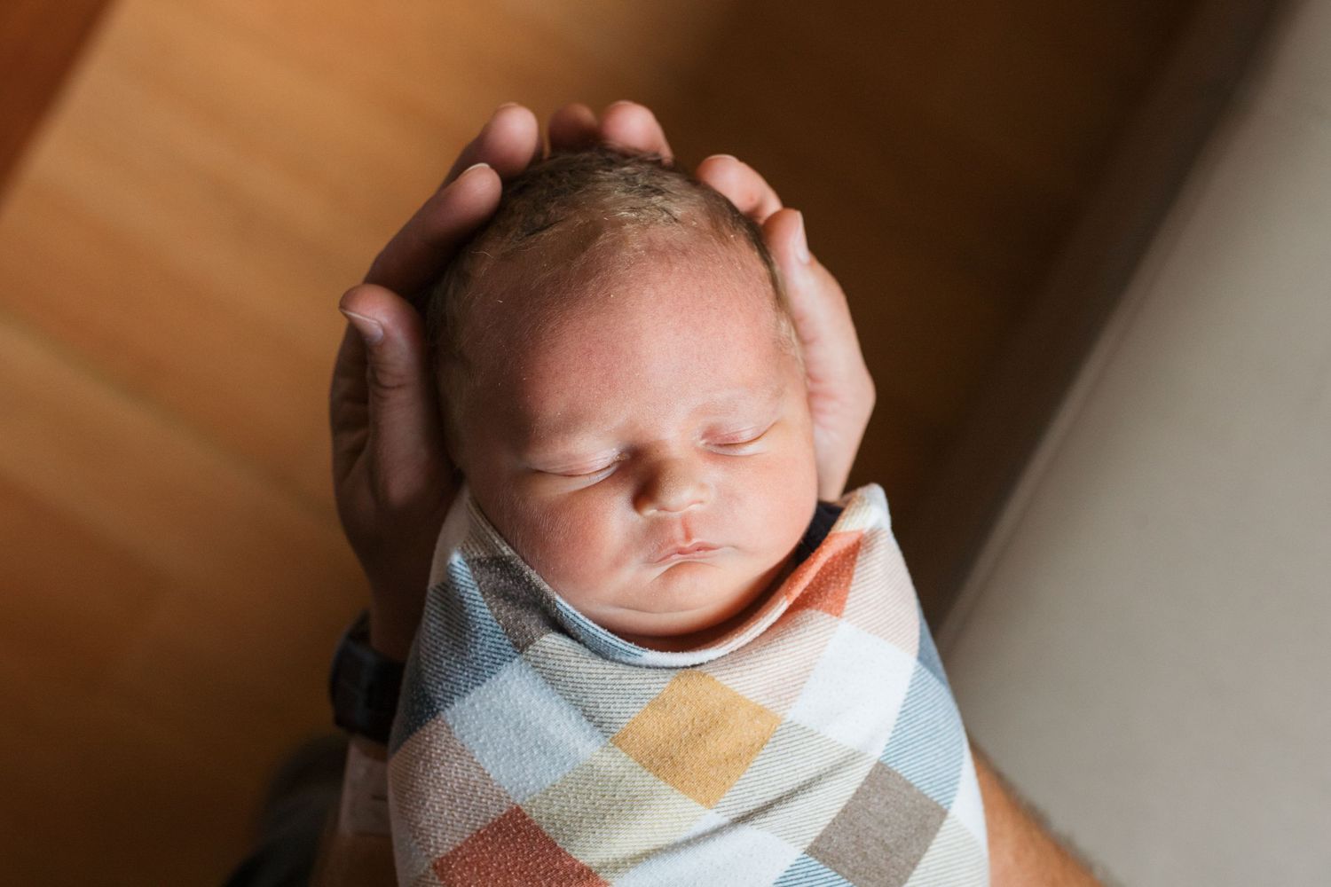 A sleeping newborn baby wrapped in a cozy swaddle blanket sleeping in parents hands Fresh 48 session in Boise, Idaho
