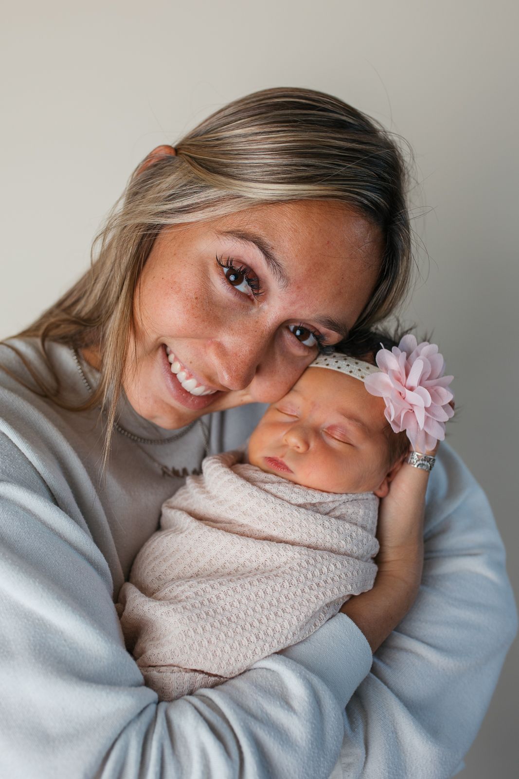 A sleeping newborn baby wearing a pink flower headband is held close by someone in a soft blue sweater  studio newborn photography Caldwell