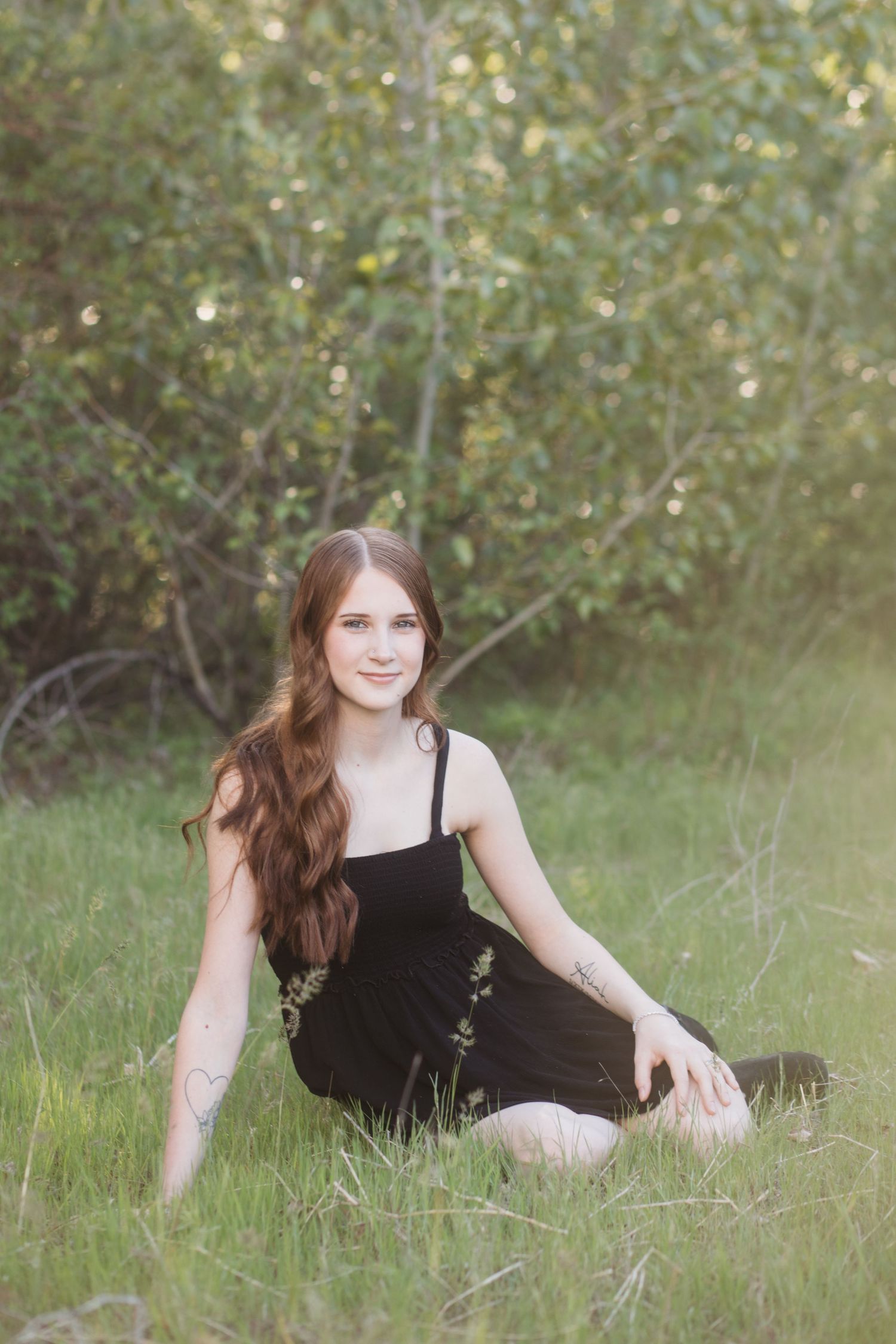 Boise senior photos of high school girl sitting in tall grass during soft golden hour outdoor session