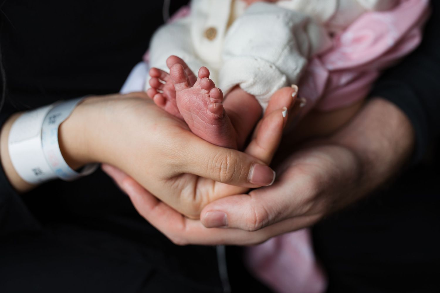 Close-up of newborn baby girl’s feet cradled in parents’ hands during Fresh 48 session