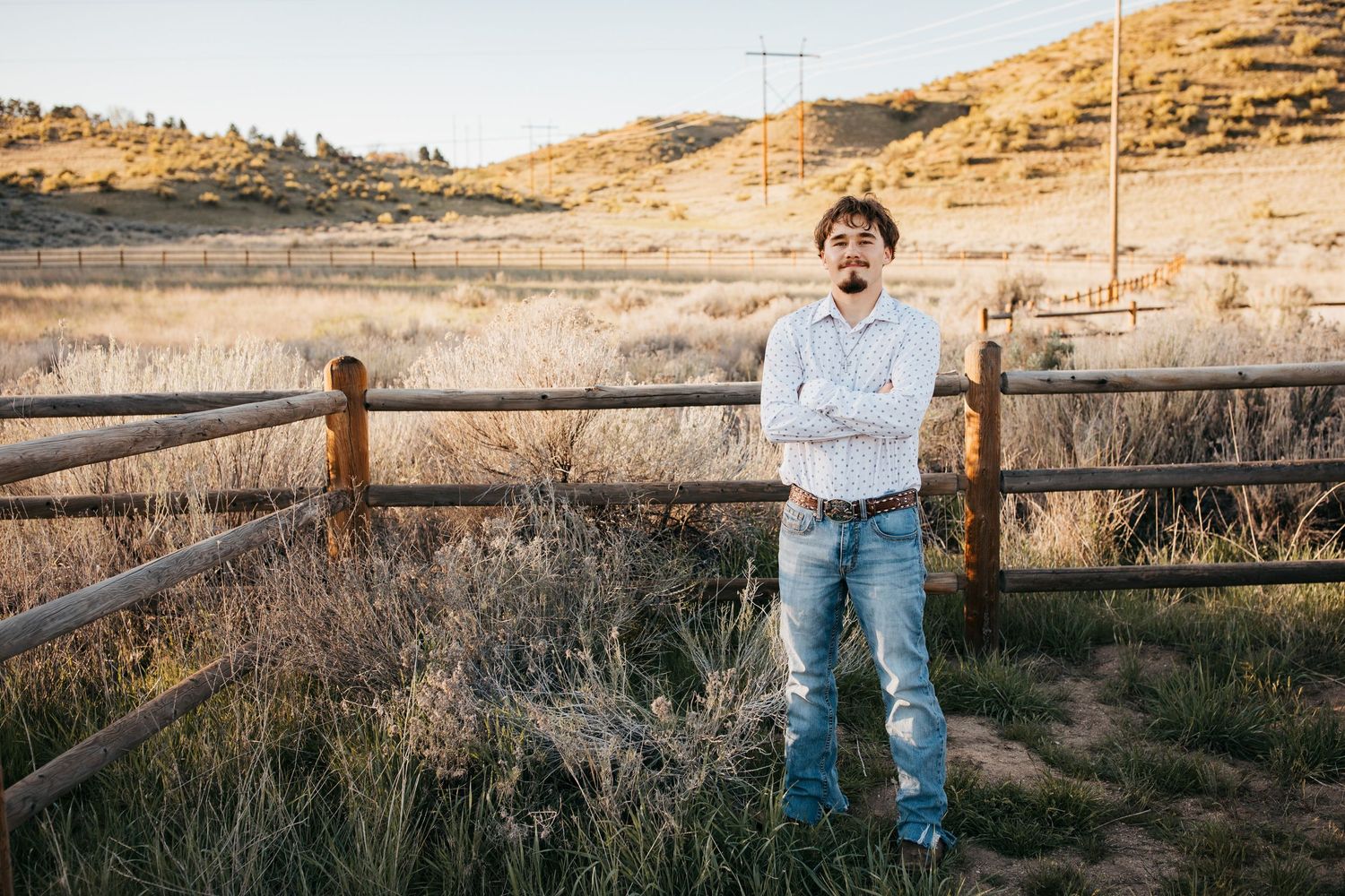 Full body senior portrait of high school boy standing by wooden fence during Boise Idaho senior photo session