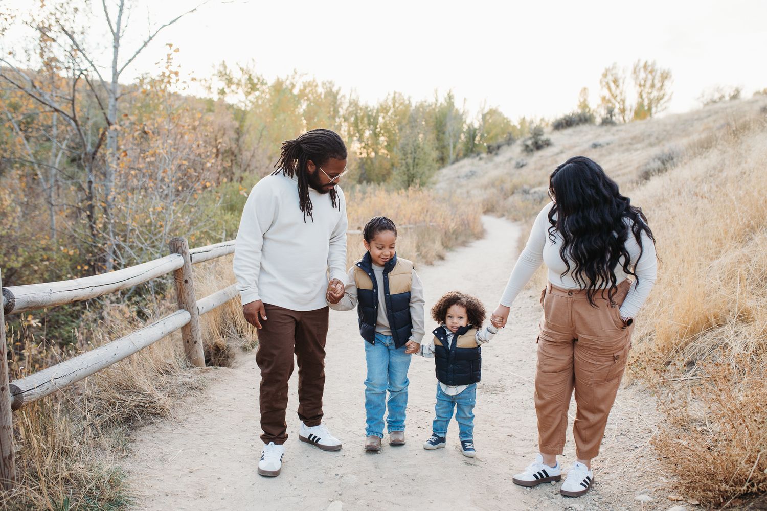A family walks together on a winding dirt path through a scenic autumn hillside during golden hour. - lifestyle family photos in Boise
