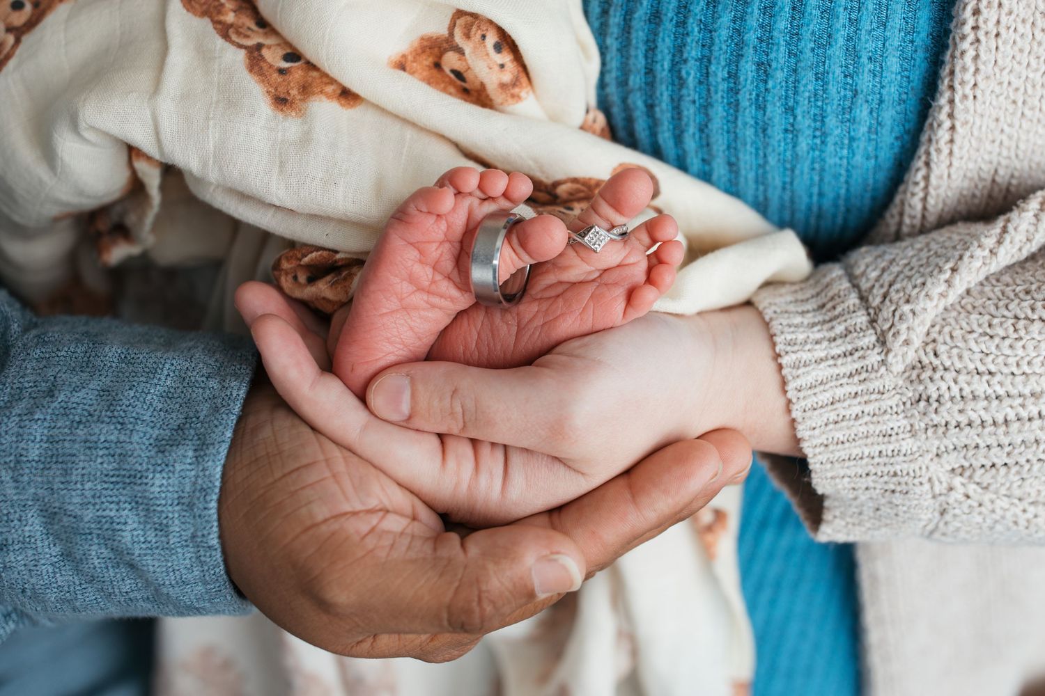 Newborn baby boy’s tiny feet cradled in his parents’ hands during studio newborn photography session